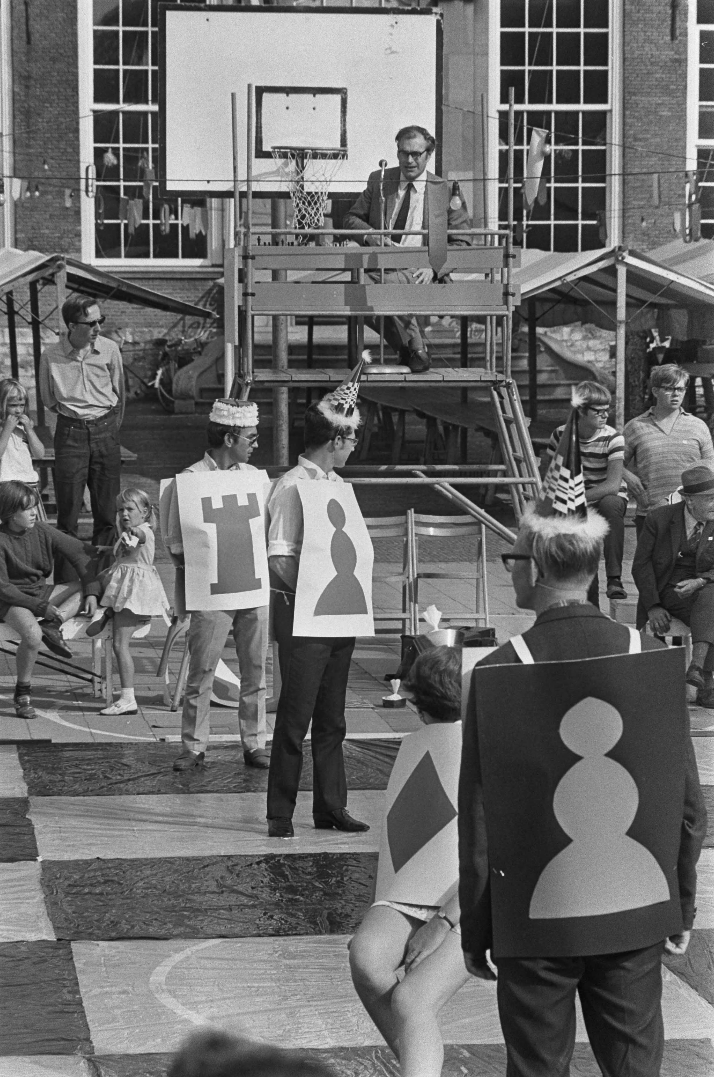 Fotocollectie Anefo — Godfried Bomans en dr. Max Euwe spelen schaakspel met levende stukken, Haarlem — Foto: Mieremet, Rob / Anefo. Licentie: Set B: Rechtenvrij / Publiek Domein. Bron: Nationaal Archief. http://hdl.handle.net/10648/aba13430-d0b4-102d-bcf8-003048976d84