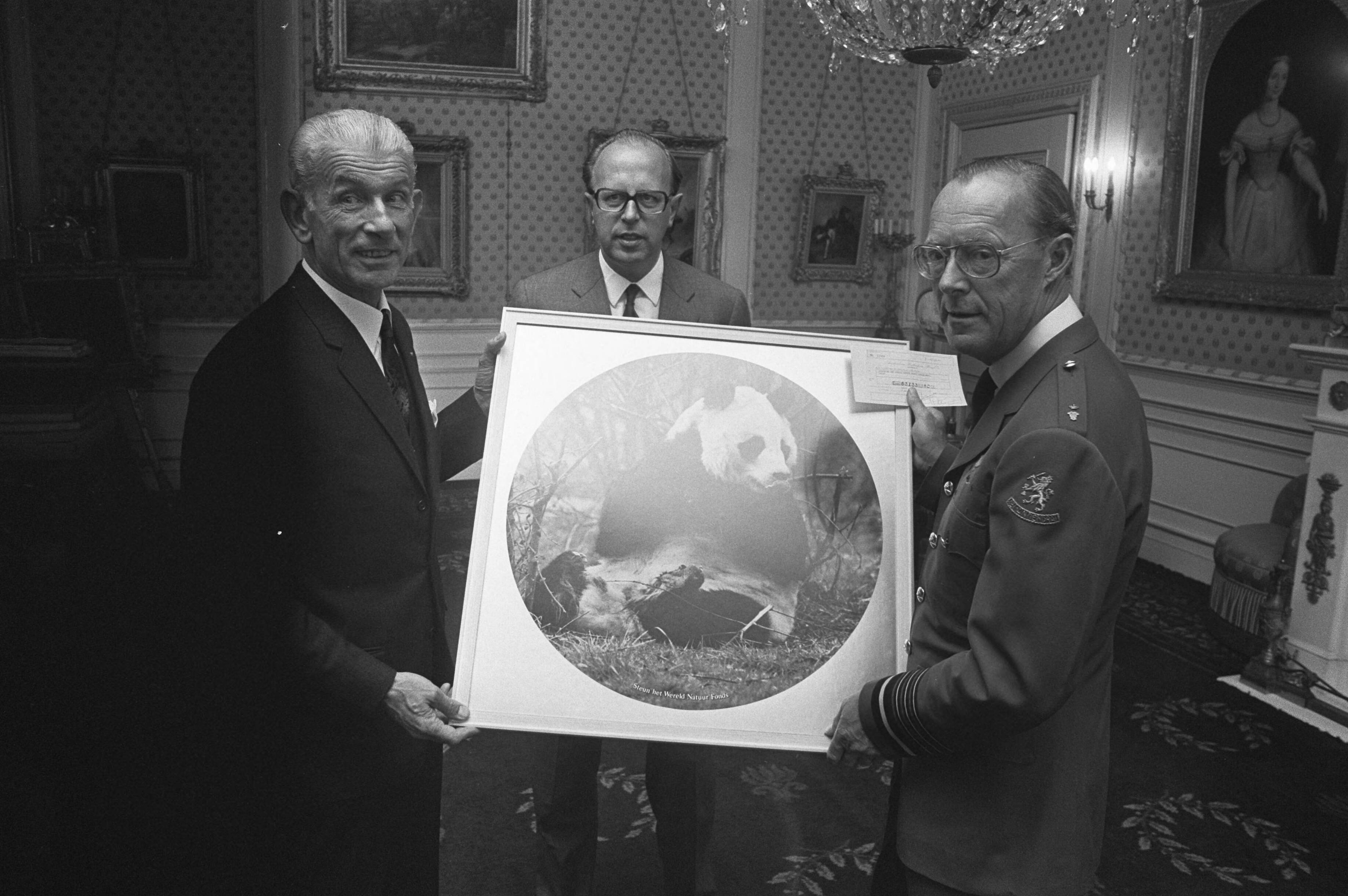 Ontvangst op Soestdijk door Prins Bernhard van een delegatie van Esso, in verband met een actie voor het Wereld Natuur Fonds — De delegatie overhandigt de prins een ingelijste foto van een pandabeer, het symbool van het Wereld Natuur Fonds — Foto: Fotograaf Onbekend / Anefo. Licentie: Set B: Rechtenvrij / Publiek Domein. Bron: Nationaal Archief. http://hdl.handle.net/10648/abe92bc8-d0b4-102d-bcf8-003048976d84