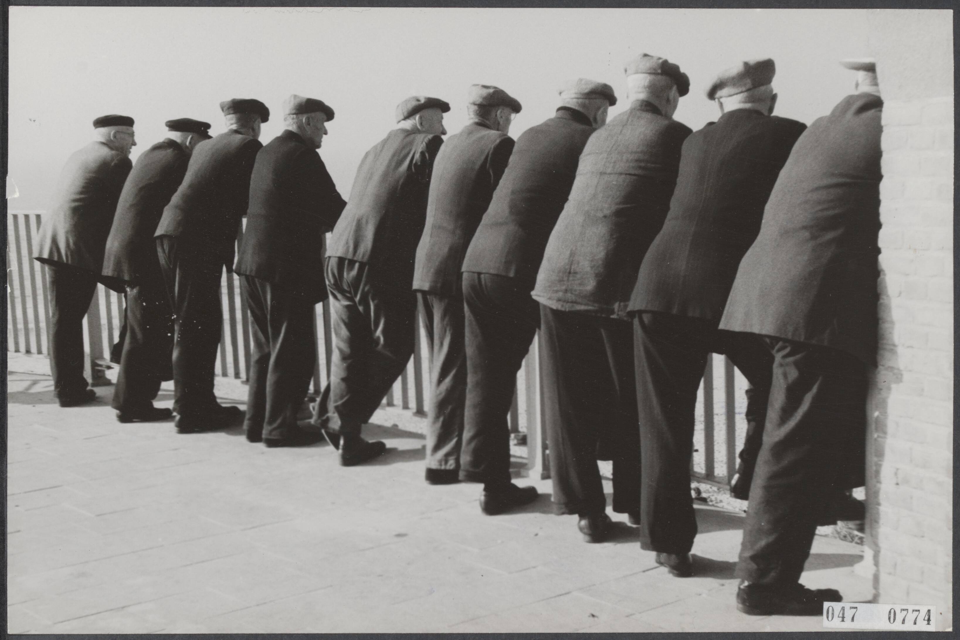 Fotocollectie Elsevier Binnenland — Rij mannen in ontspannen houding leunend op een hek in Zandvoort — Foto: Fotograaf Onbekend / Anefo. Licentie: Set B: Rechtenvrij / Publiek Domein. Bron: Nationaal Archief. http://hdl.handle.net/10648/ae004518-d0b4-102d-bcf8-003048976d84