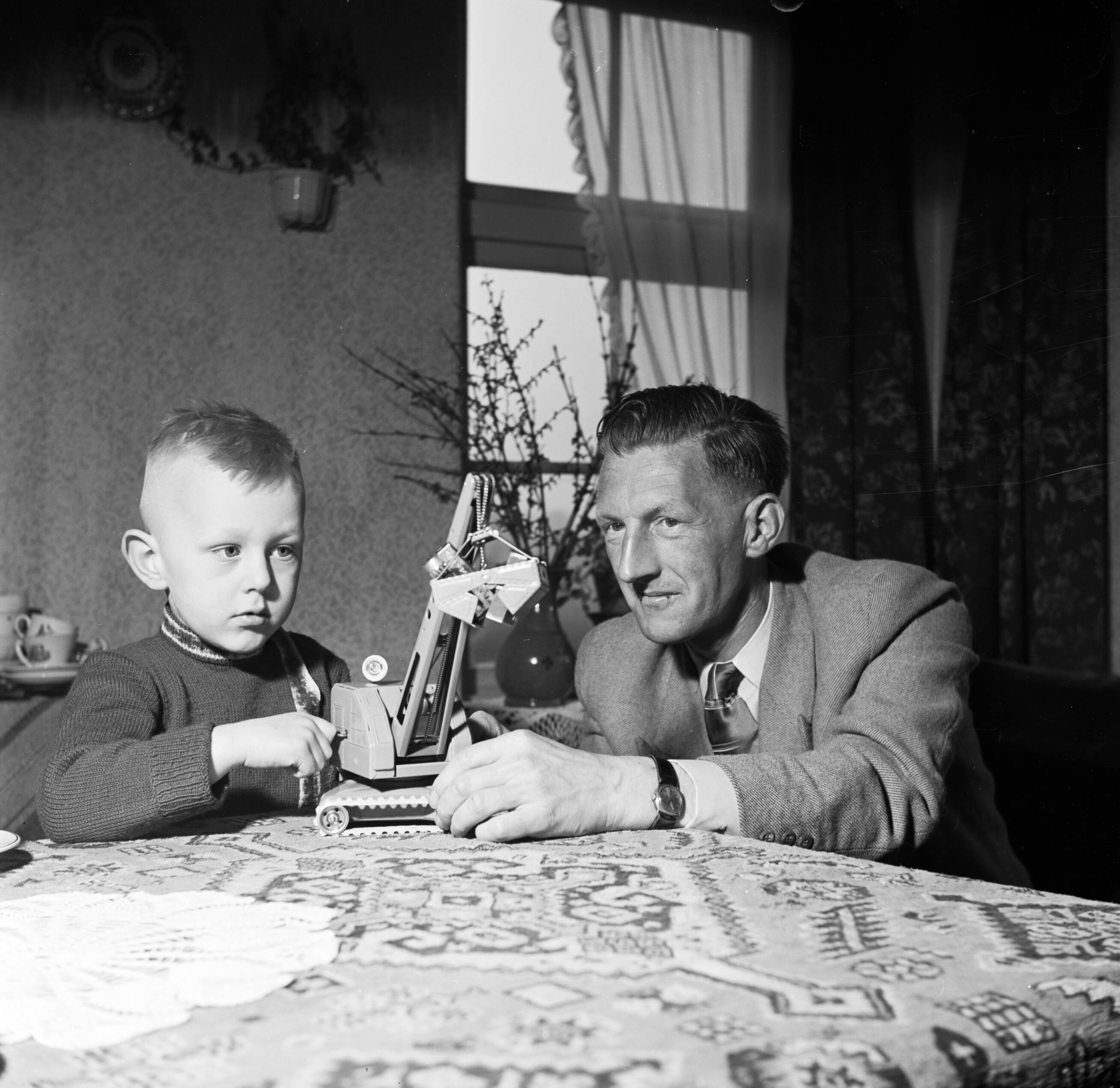 Fotocollectie Van de Poll — Gerard met zijn vierjarig zoontje aan tafel met een speelgoedhijskraan — Foto: Poll, Willem van de. Licentie: Set B: Rechtenvrij / Publiek Domein. Bron: Nationaal Archief. http://hdl.handle.net/10648/aeccce80-d0b4-102d-bcf8-003048976d84