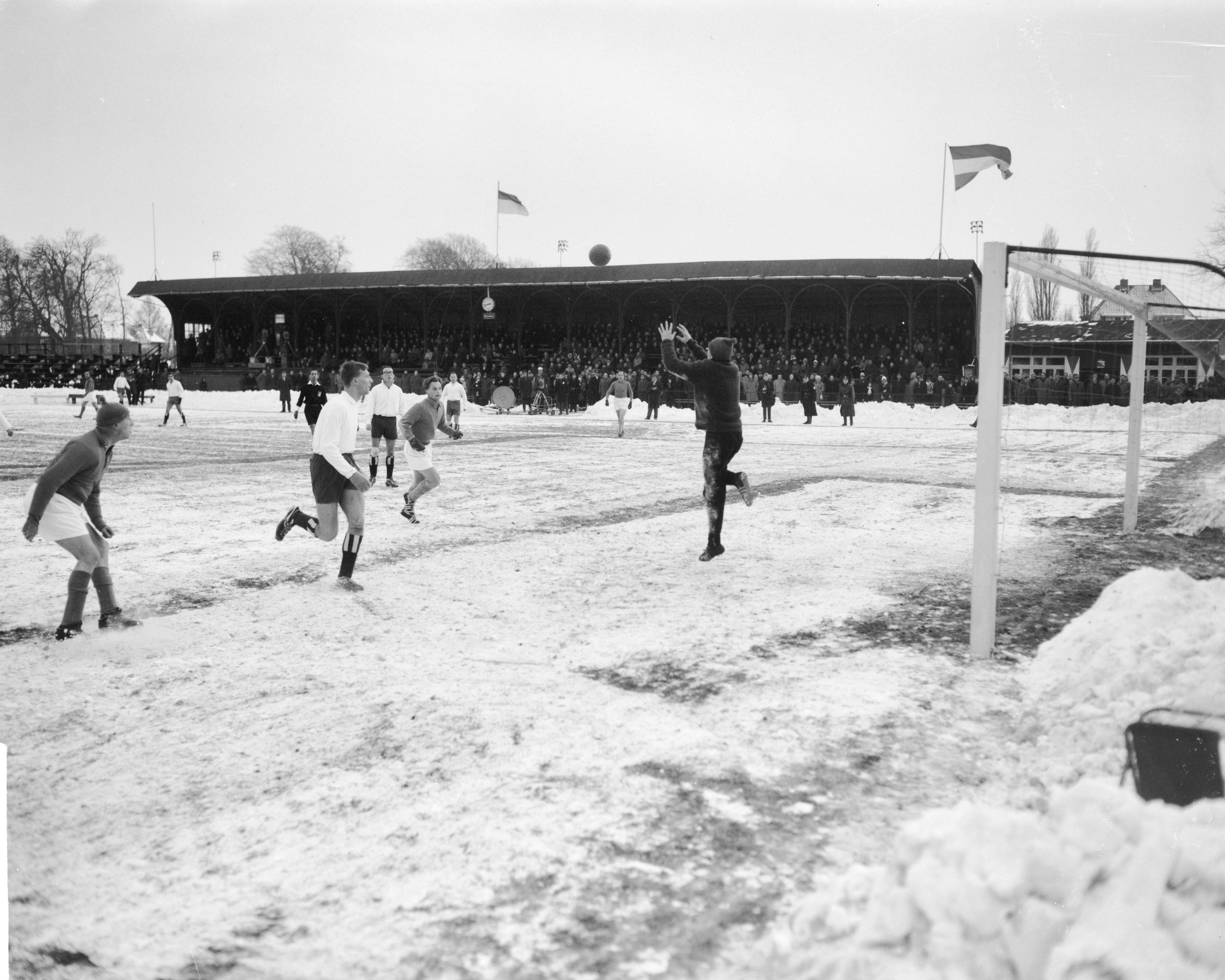 Fotocollectie Anefo — Traditionele nieuwjaars voetbalwedstrijd tussen de Koninklijke HFC en Oud-Internationals 2-8. Spelmoment. HFC keeper Guus van der Meulen jr. springt naar de bal. Links met ijsmuts Wim Roosen, in het midden Piet Groeneveld, rechts Arie de Vroet — Foto: Bilsen, Joop van / Anefo. Licentie: Set B: Rechtenvrij / Publiek Domein. Bron: Nationaal Archief. http://hdl.handle.net/10648/aa2462a8-d0b4-102d-bcf8-003048976d84