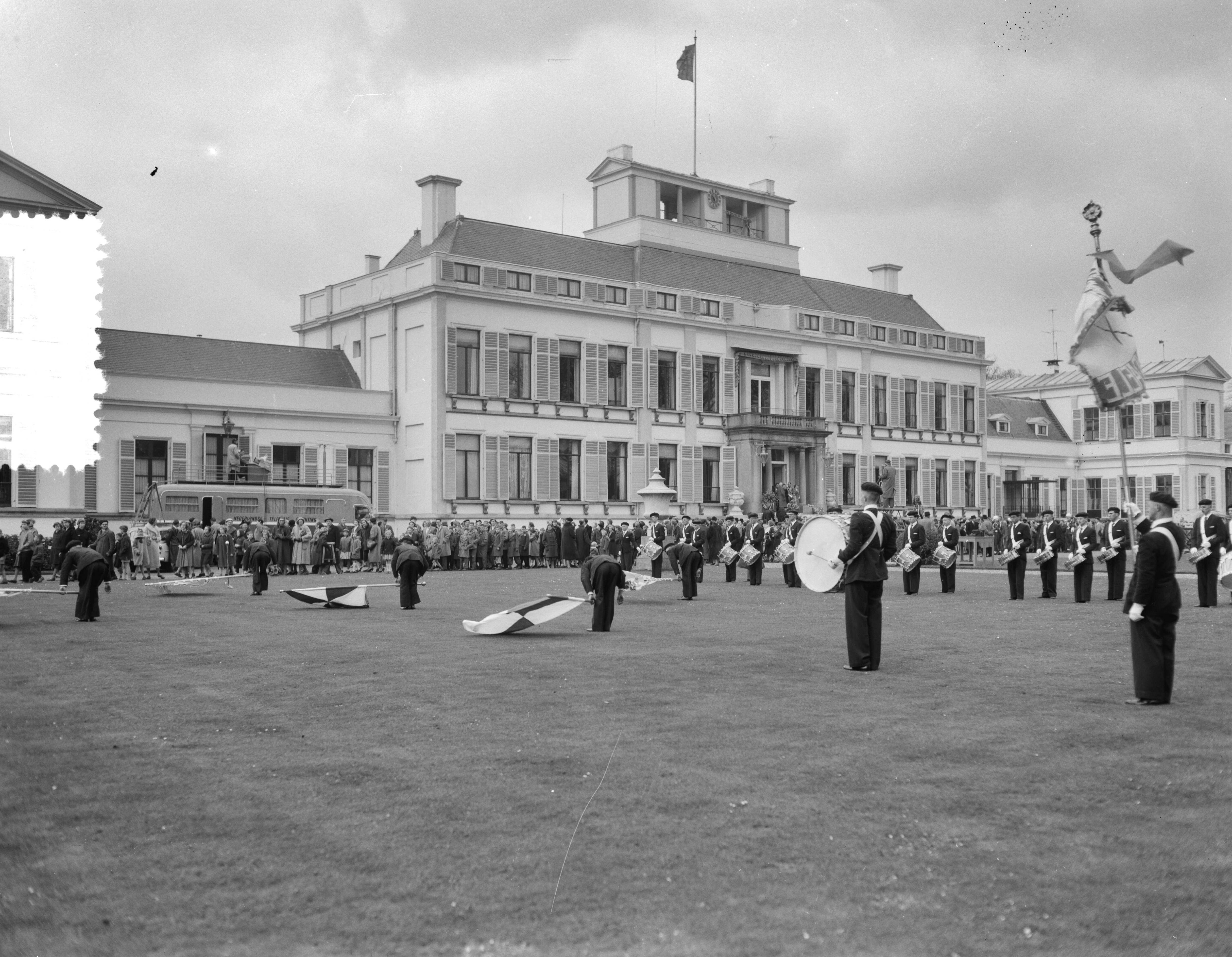 Koninginnedag 1956 — Defilé langs paleis Soestdijk ter gelegenheid van de verjaardag van koningin Juliana. Muziekkorps met vendelzwaaiers op het gazon voor paleis Soestdijk — Foto: Noske, J.D. / Anefo. Licentie: Set B: Rechtenvrij / Publiek Domein. Bron: Nationaal Archief. http://hdl.handle.net/10648/a94705d4-d0b4-102d-bcf8-003048976d84
