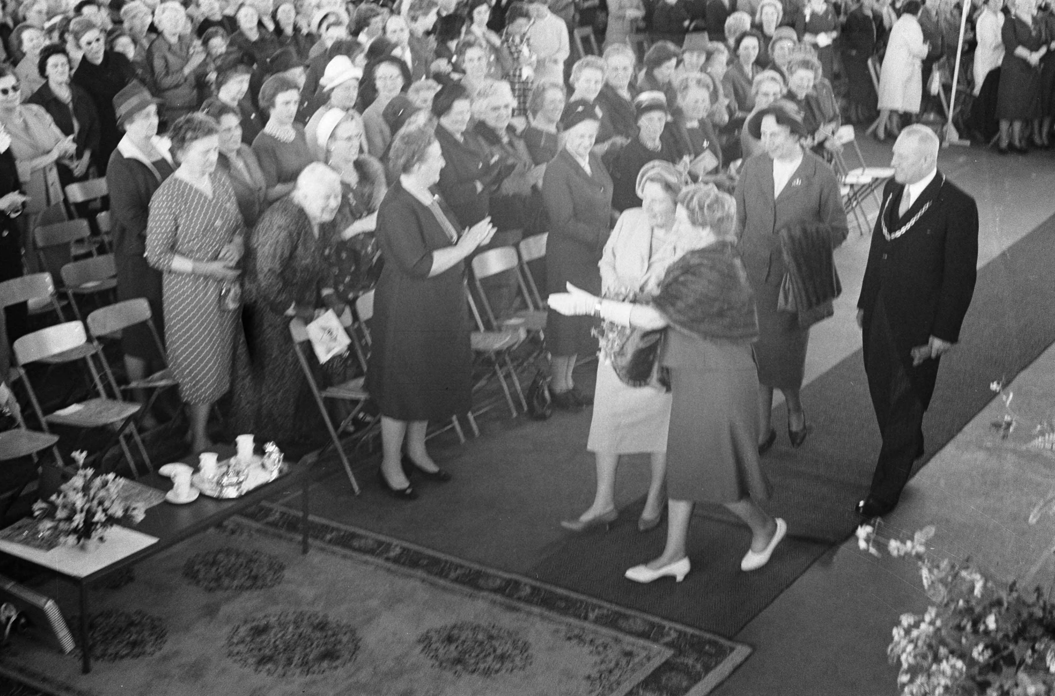 Fotocollectie Anefo — Koningin Juliana is aanwezig bij de viering van het 50-jarig bestaan van de Nederlandse Vereniging van Huisvrouwen in de Expohal te Hilversum. Aankomst in gezelschap van mevr. W.A. Boot-Colijn, echtgenote van burgemeester Boot die achter hen loopt, samen met mevr. G.H. Keyser-Hardick, presidente van het hoofdbestuur — Foto: Fotograaf Onbekend / Anefo. Licentie: Set B: Rechtenvrij / Publiek Domein. Bron: Nationaal Archief. http://hdl.handle.net/10648/aa02b518-d0b4-102d-bcf8-003048976d84