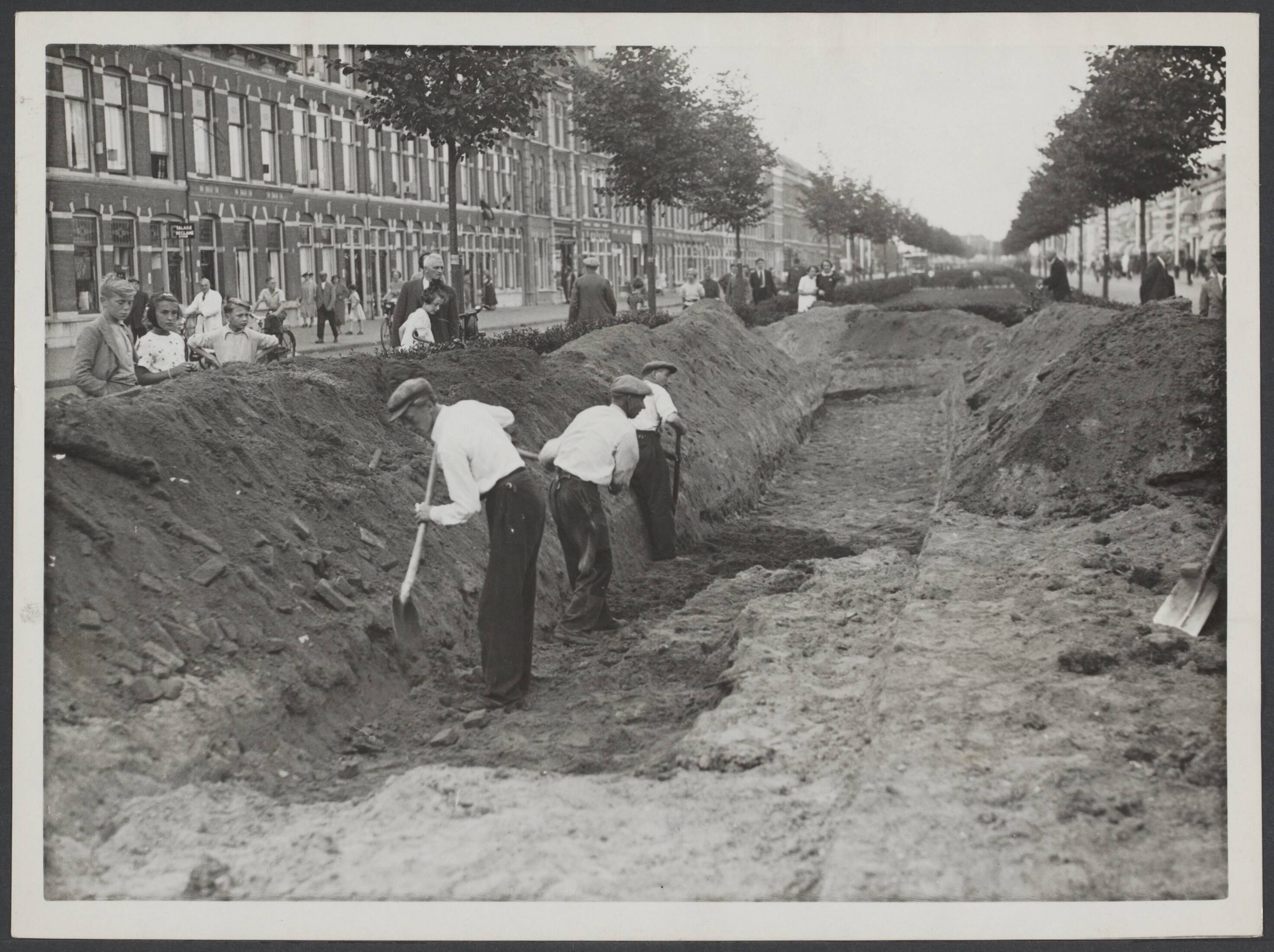 BVD. Bescherming bevolking, enz. Nederland. — Den Haag, 30 augustus 1939. In Den Haag is men druk bezig op een groot aantal plaatsen schuilloopgraven te maken, om in geval van nood de bevolking te beveiligen. Op de Loosduinseweg waar men o.a. met een der schuilloopgraven bezig is welke een lengte krijgt van 60 meter — Foto: N.V. Polygoon. Licentie: Set B: Rechtenvrij / Publiek Domein. Bron: Nationaal Archief. http://hdl.handle.net/10648/175ed486-7277-da69-5dd1-c0ef1503f7b4