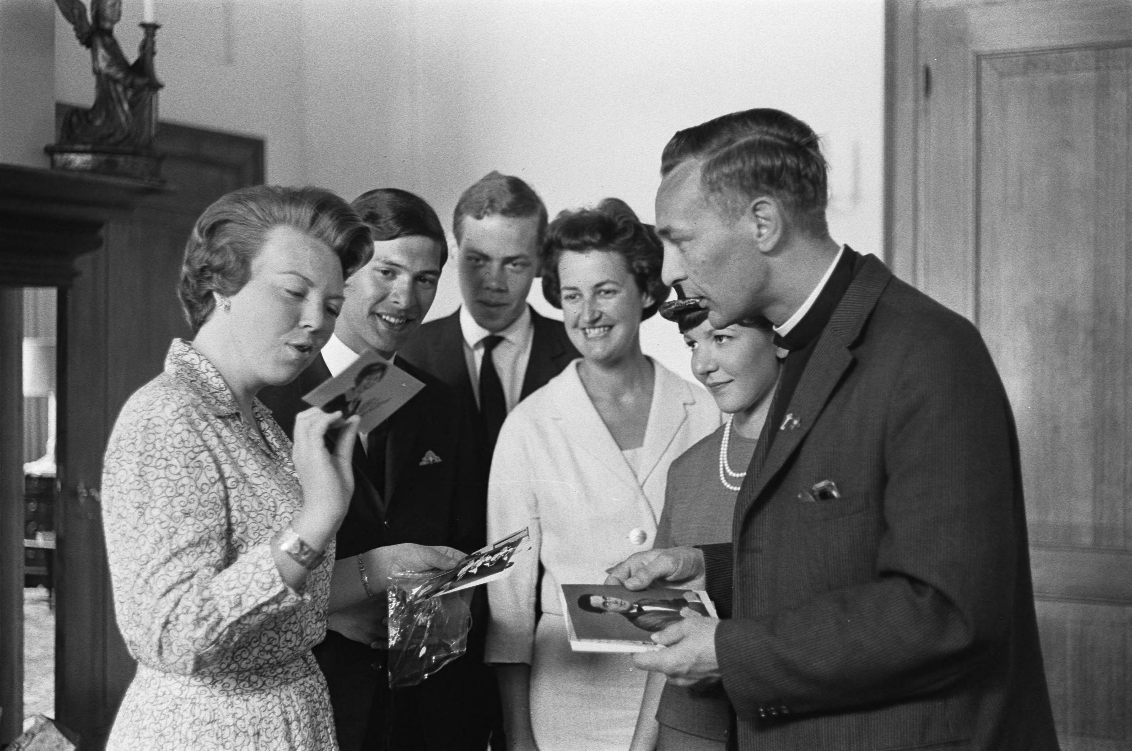 Fotocollectie Anefo — Prinses Beatrix heeft op Kasteel Drakensteyn het actie-comité "Dousadsj" ontvangen, v.l.n.r. Prinses Beatrix , dhr. Rompius, Miss Dousadsj [Adele Rompius-Sadrille], P. van Bueren, pater Werenfried Stokman en mevrouw J. Rigby (penningmeester Europese werkgroep). Prins Beatrix bekijkt een van de overhandigde foto's — Foto: Pot, Harry / Anefo. Licentie: Set B: Rechtenvrij / Publiek Domein. Bron: Nationaal Archief. http://hdl.handle.net/10648/aa39373c-d0b4-102d-bcf8-003048976d84