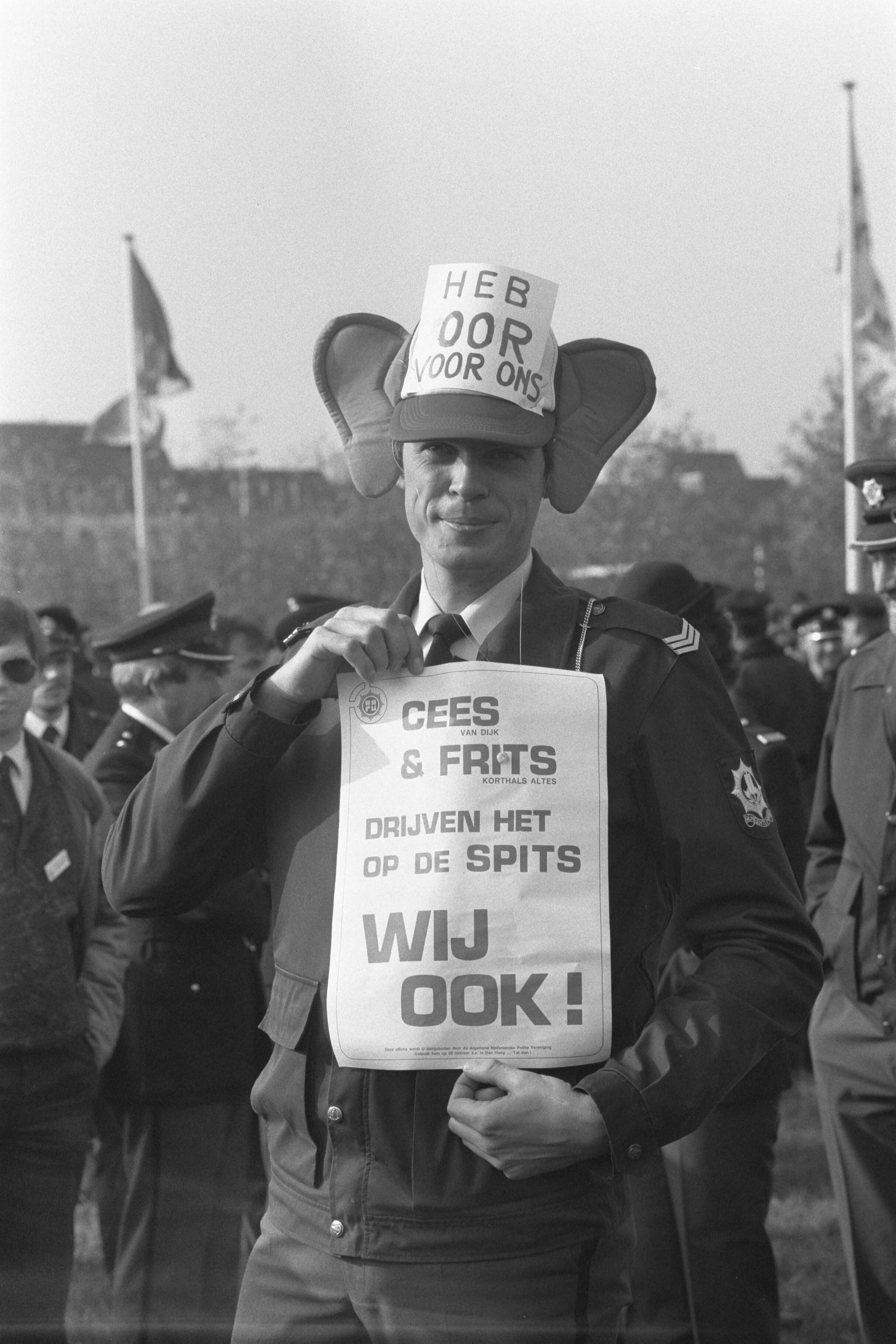 Fotocollectie Anefo — Politie demonstreert in Den Haag tegen bezuinigingen; politiemensen met affiches en oren — Foto: Croes, Rob C. / Anefo. Licentie: Set B: Rechtenvrij / Publiek Domein. Bron: Nationaal Archief. http://hdl.handle.net/10648/ad65725e-d0b4-102d-bcf8-003048976d84