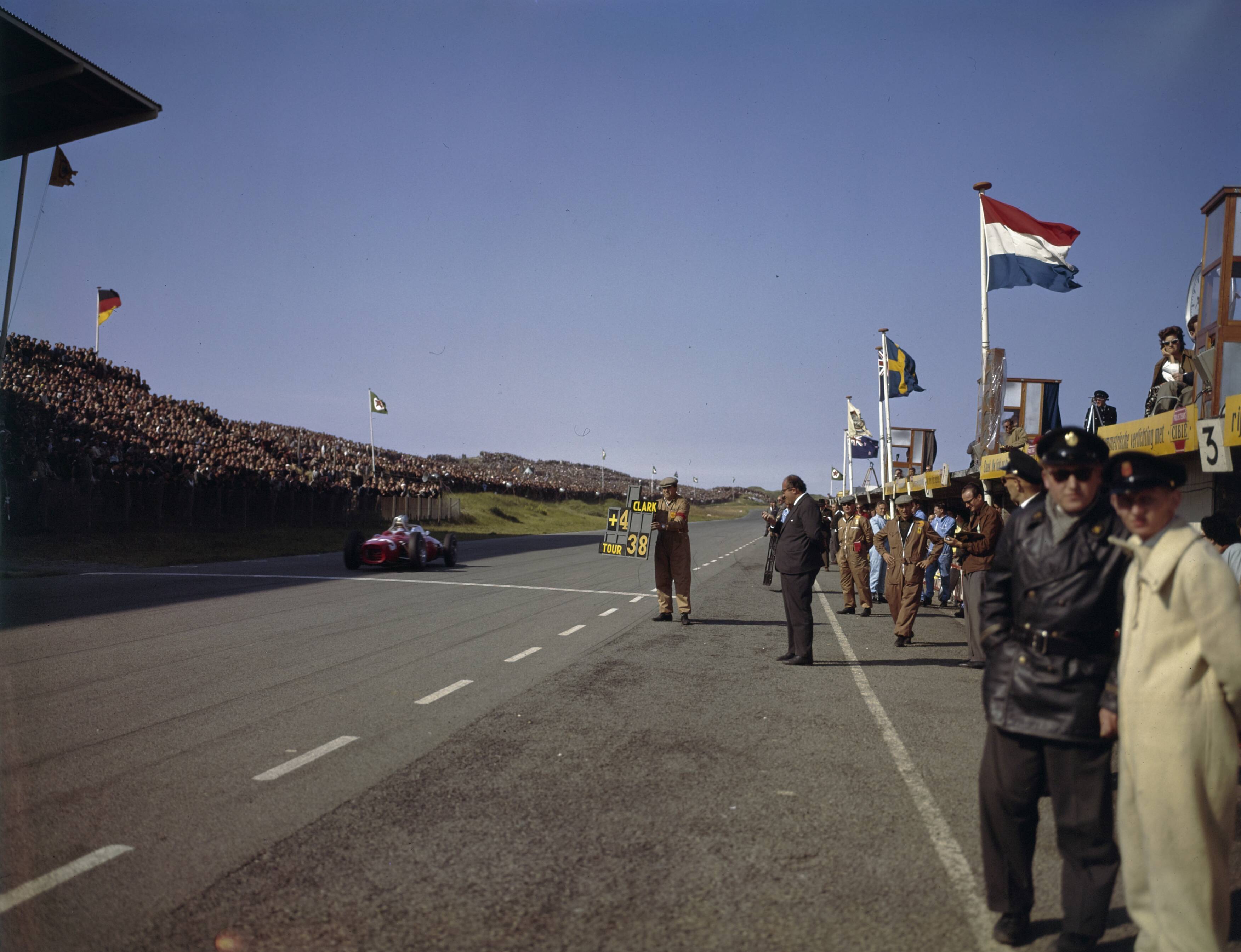 Fotocollectie Anefo — [Grand Prix Zandvoort 1961. Man houdt bord op met mededeling "Clark +4 tour 38. Een raceauto met nummer 3 (Wolfgang von Trips, de latere winnaar) passeert de finishlijn] — Foto: Fotograaf Onbekend / Anefo. Licentie: Set B: Rechtenvrij / Publiek Domein. Bron: Nationaal Archief. http://hdl.handle.net/10648/ad8cd326-d0b4-102d-bcf8-003048976d84
