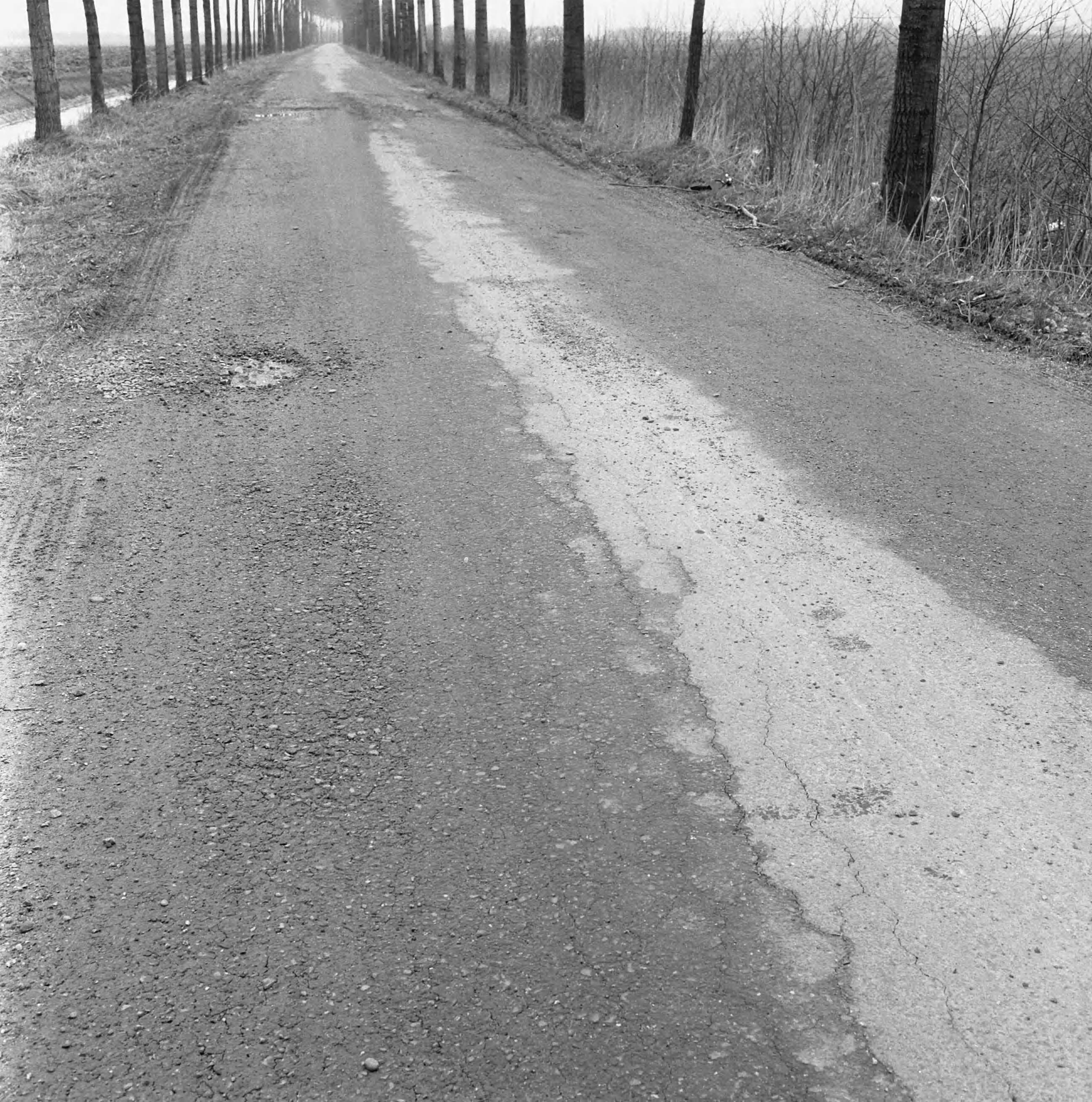 Fotocollectie Nederlandse Heidemaatschappij — Ruilverkaveling Vleuten. Joostenlaan. Met betonmolen in augustus 1956 gestabiliseerde gedeelte van de oude grind-sintelverharding op klei-ondergronf, met deklaagje van teersteenslag. Funderingsdikte 12 1/2 cm. Toestand op 3 maart 1958. Deplorabel na toevallig zwaar en intensief zandtransport — Foto: Wüllschleger, [...] / Heidemij. Licentie: Set B: Rechtenvrij / Publiek Domein. Bron: Nationaal Archief. http://hdl.handle.net/10648/ae7143da-d0b4-102d-bcf8-003048976d84