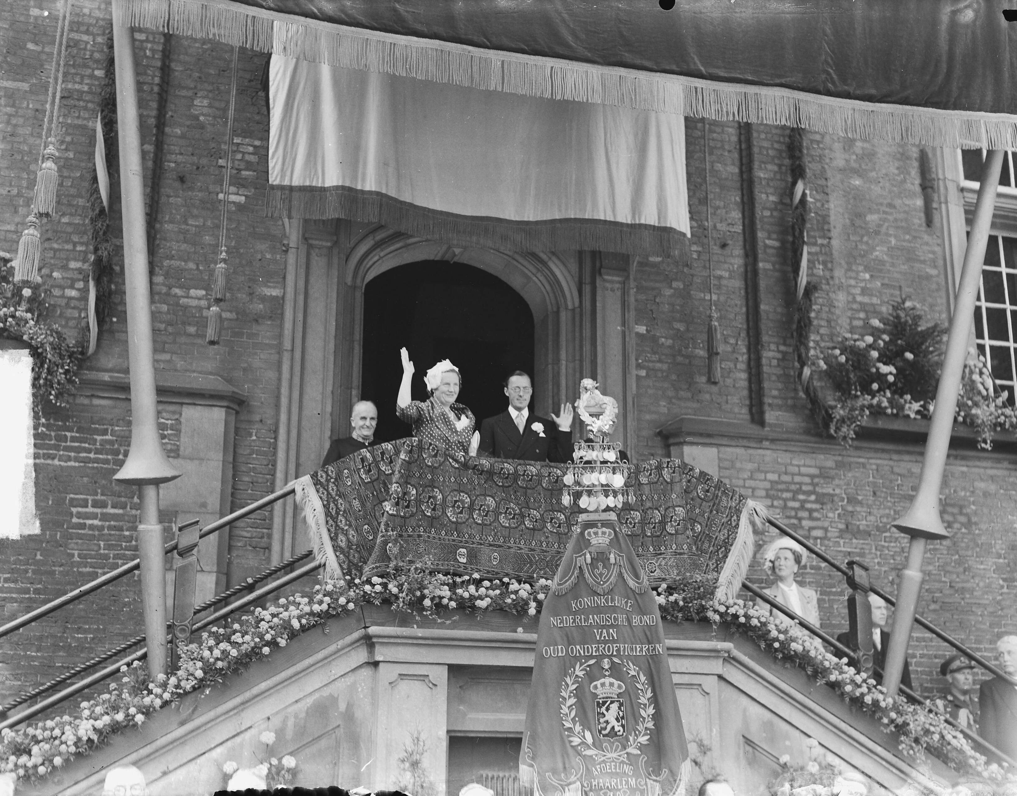 Koningin Juliana en prins Bernhard in Haarlem — Koningin Juliana en prins Bernhard op het bordes van het raadhuis — Foto: Bilsen, Joop van / Anefo. Licentie: Set B: Rechtenvrij / Publiek Domein. Bron: Nationaal Archief. http://hdl.handle.net/10648/a8cb27c0-d0b4-102d-bcf8-003048976d84