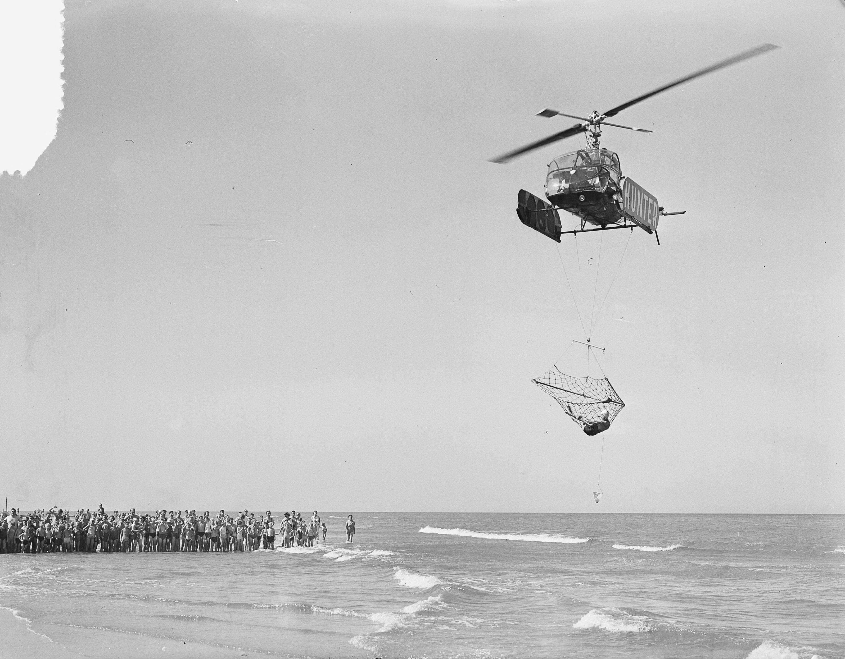 Fotocollectie Anefo — Demonstratie helicopter van Aero Ypenburg met nieuw reddingsnet bij het strand van Scheveningen. In het net bevind zich de 14-jarige "drenkelinge" Marie-Antoinette Verlinden — Foto: Bilsen, Joop van / Anefo. Licentie: Set B: Rechtenvrij / Publiek Domein. Bron: Nationaal Archief. http://hdl.handle.net/10648/a939fb64-d0b4-102d-bcf8-003048976d84
