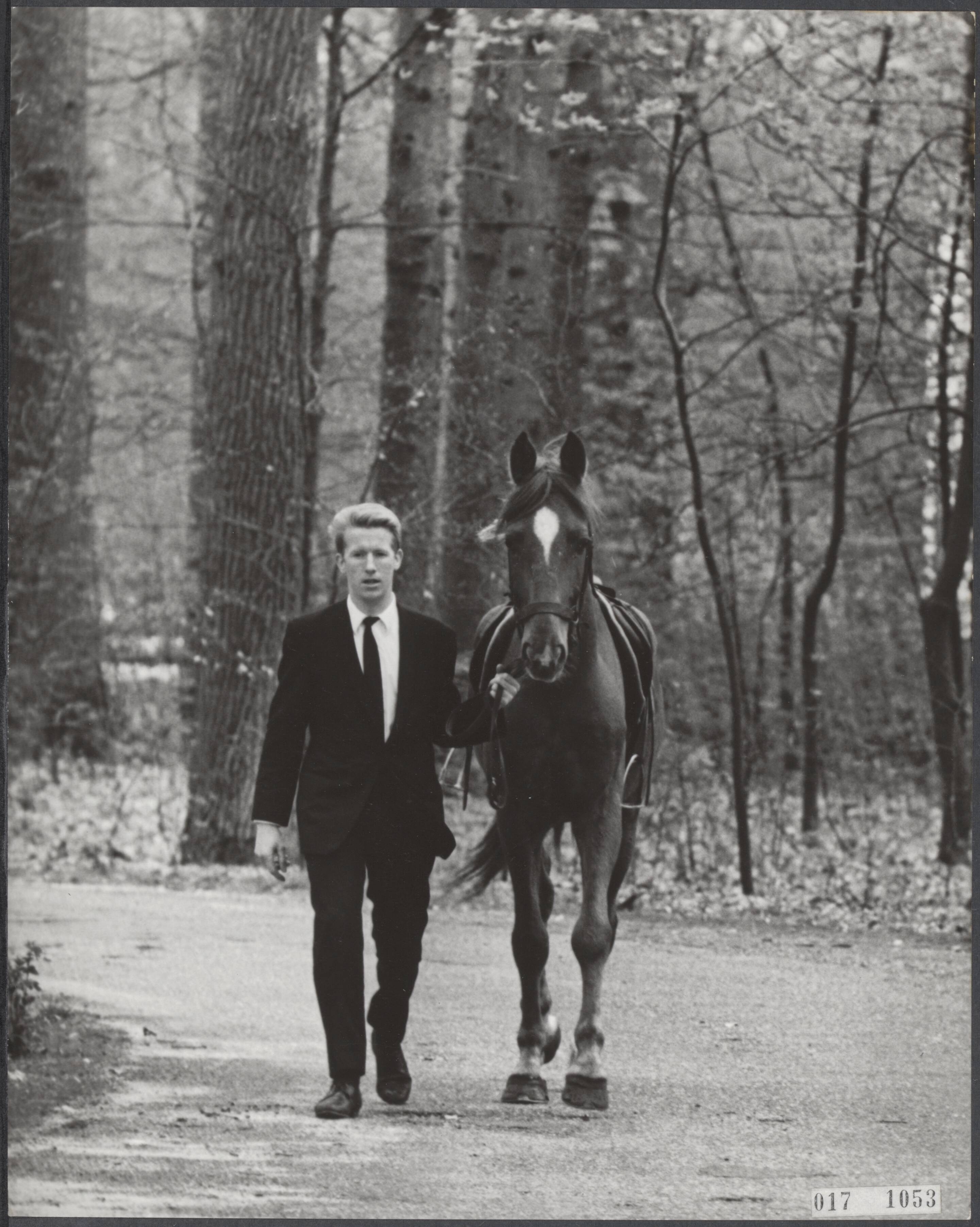 Fotocollectie Elsevier Binnenland — Even na het middaguur werd de paleiswacht van kasteel Drakensteyn opgeschrikt door een op hol geslagen paard, dat in volle ren de poort binnen draafde. Erop zag André Gorel, ober in hotel De Lage Vuursche, die het paard in de stal zouzetten nadat mej. Diny Meewis er al moeilijkheden mee had. André Gorel loopt naast het gevangen paard in de tuin van Drakensteyn terug naar de poort — Foto: Koch, Eric / Anefo. Licentie: Set B: Rechtenvrij / Publiek Domein. Bron: Nationaal Archief. http://hdl.handle.net/10648/adbfd816-d0b4-102d-bcf8-003048976d84