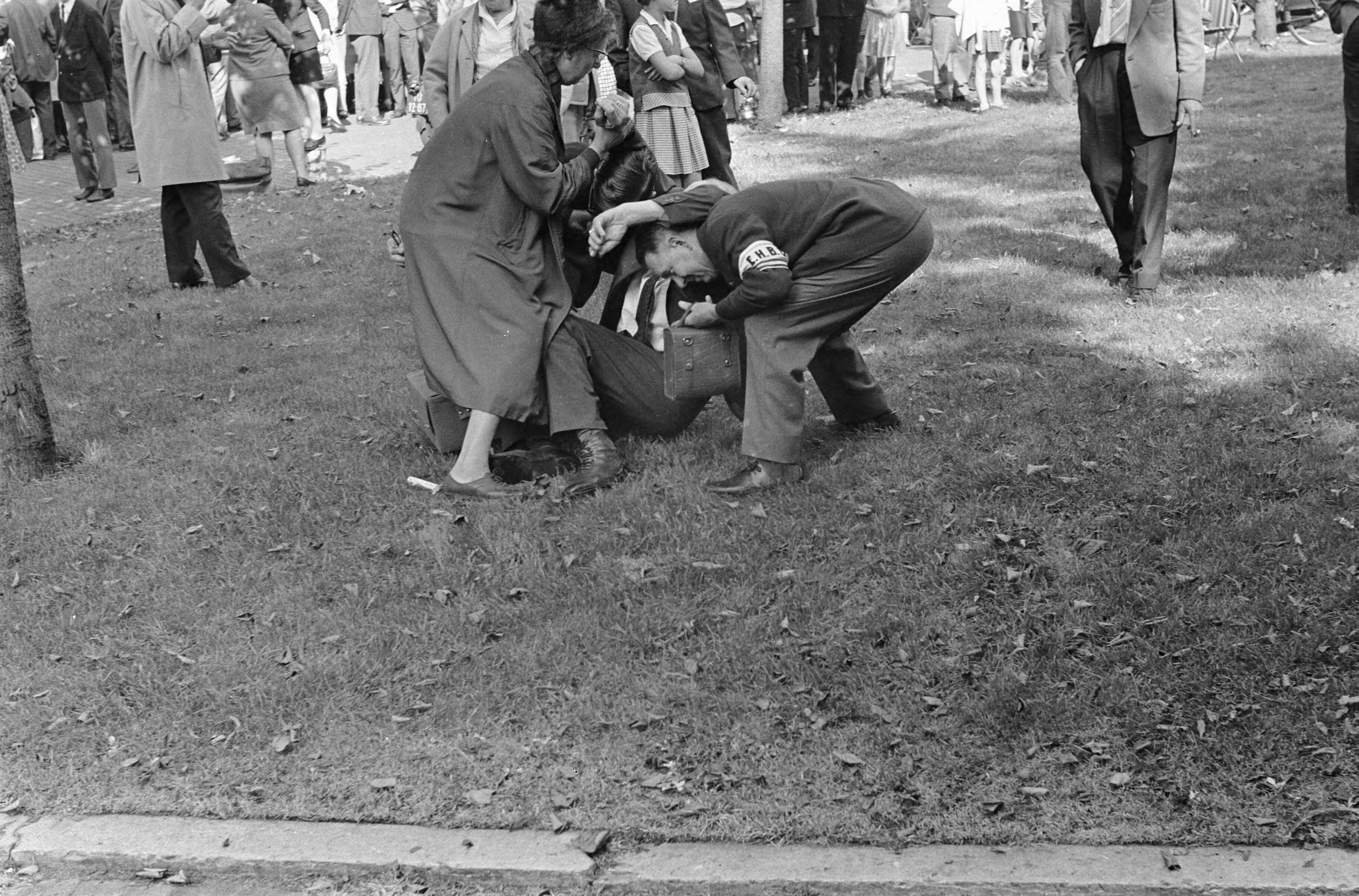 Protesterende Amsterdamse Provo's tijdens Prinsjesdag 1966 in Den Haag — Enkele omstanders verlenen hulp aan een gewonde — Foto: Fotograaf Onbekend / Anefo. Licentie: Set B: Rechtenvrij / Publiek Domein. Bron: Nationaal Archief. http://hdl.handle.net/10648/aafd3f1a-d0b4-102d-bcf8-003048976d84