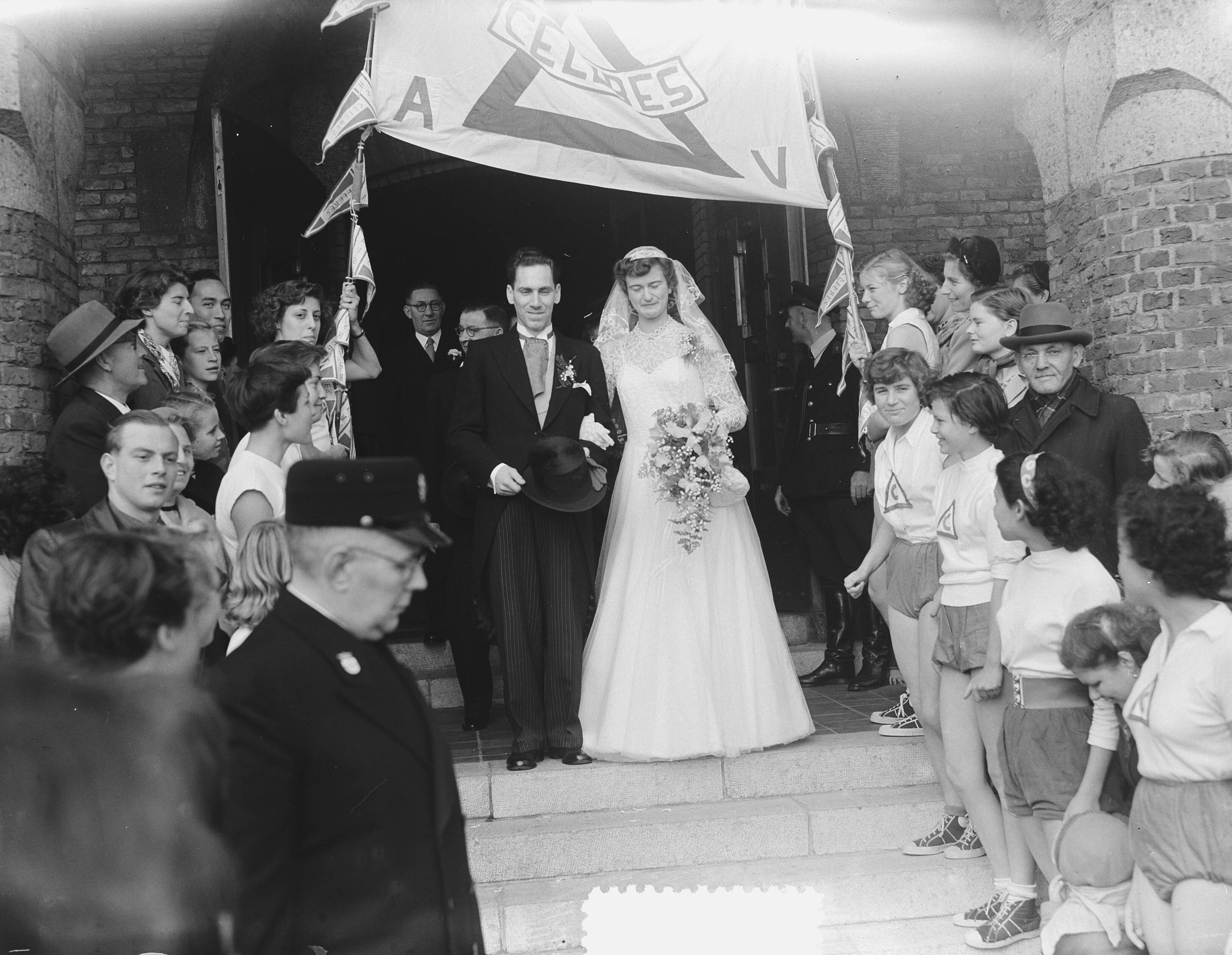 Fotocollectie Anefo — Huwelijk scheepswerktuigkundige Jan van Duyne en atlete Puck Brouwer te Leidschendam [het bruidspaar loopt door een erehaag van Celebes-atleten] — Foto: Behrens, Herbert F. / Anefo. Licentie: Set B: Rechtenvrij / Publiek Domein. Bron: Nationaal Archief. http://hdl.handle.net/10648/a915efd0-d0b4-102d-bcf8-003048976d84