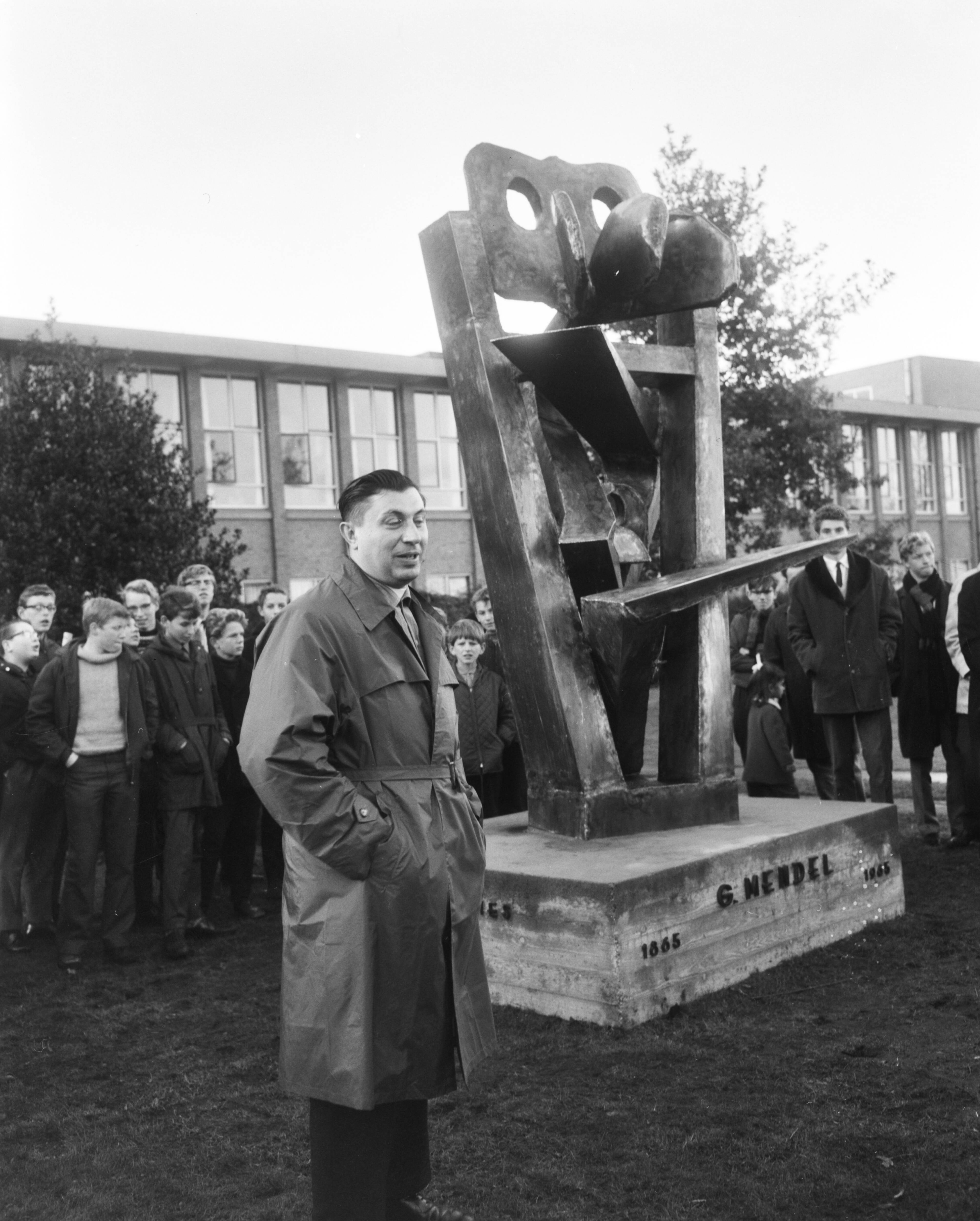 Professor dr. J. Heimans-monument, ontworpen door pater Thomas Roder, onthuld op het terrein van het Mendelcollege te Haarlem, voorstellend de erfelijkheidsleer — Pater Thomas Roder(beeldhouwer) terwijl hij naast het beeld staat — Foto: Bilsen, Joop van / Anefo. Licentie: Set B: Rechtenvrij / Publiek Domein. Bron: Nationaal Archief. http://hdl.handle.net/10648/aacba266-d0b4-102d-bcf8-003048976d84