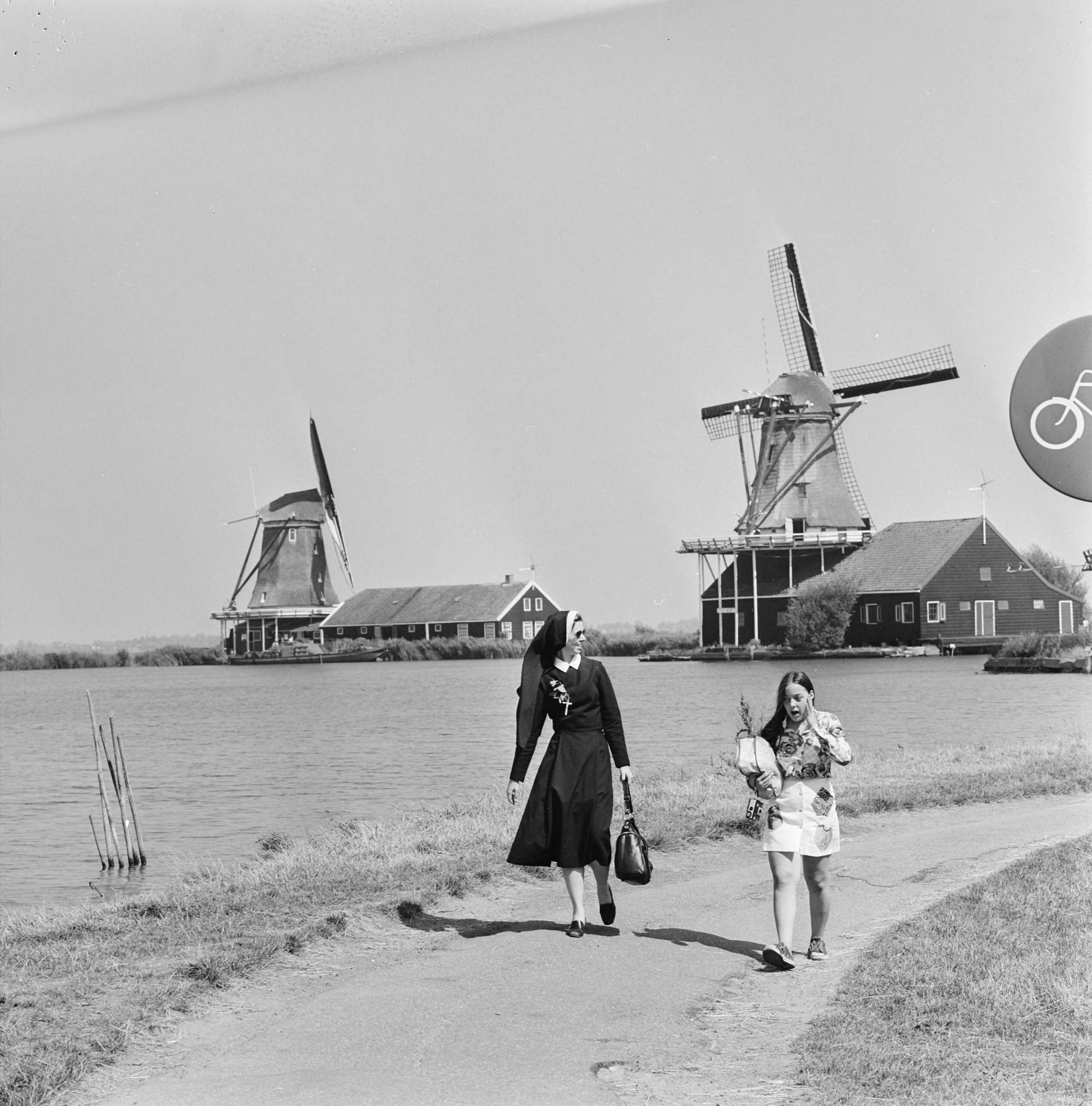 De Zaanse Schans met molens — Een paar Noord-Hollandse molens bij een meer. Op het voetpad een non en een meisje — Foto: Mieremet, Rob / Anefo. Licentie: Set B: Rechtenvrij / Publiek Domein. Bron: Nationaal Archief. http://hdl.handle.net/10648/ac6eed94-d0b4-102d-bcf8-003048976d84