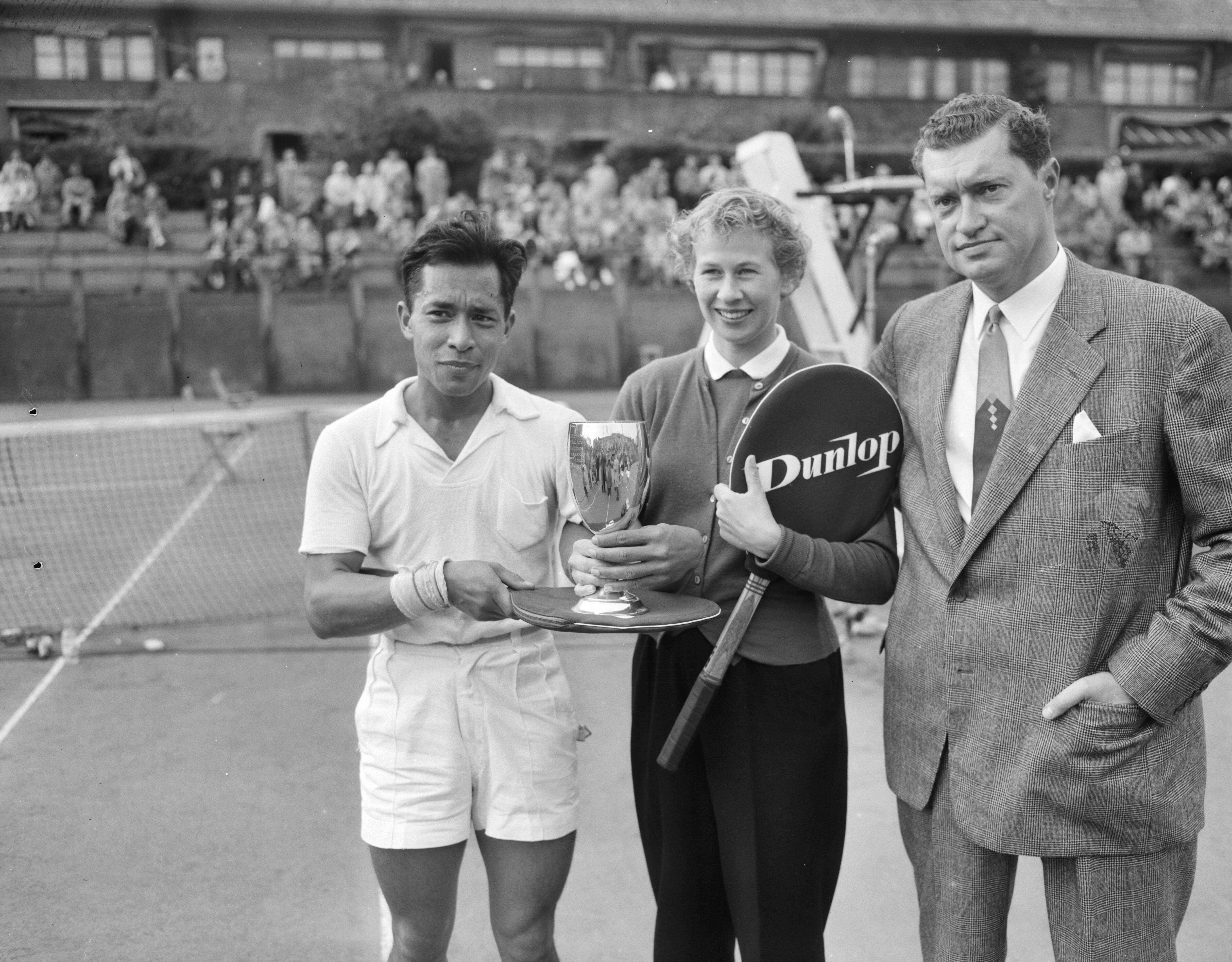 Fotocollectie Anefo — Nederlandse tenniskampioenschappen op de METS-banen. Winnaars heren en dames enkelspel Lex Karamoy en Jopie Roos-van de Wal. Rechts KNLTB voorzitter Wilton — Foto: Noske, J.D. / Anefo. Licentie: Set B: Rechtenvrij / Publiek Domein. Bron: Nationaal Archief. http://hdl.handle.net/10648/a94d8738-d0b4-102d-bcf8-003048976d84