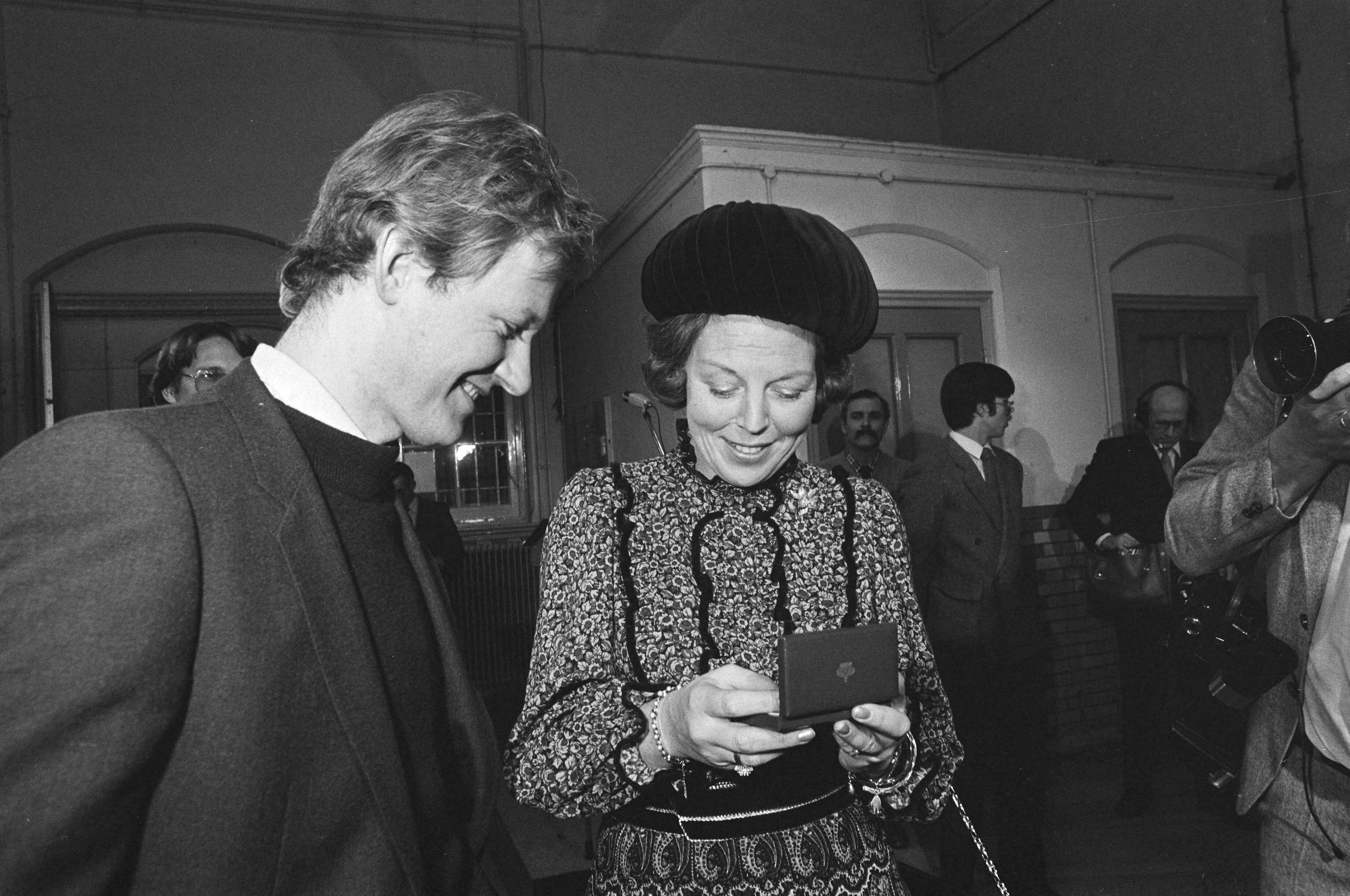 Fotocollectie Anefo — Koningin Beatrix slaat ook eerste nieuwe guldens in Rijksmunt te Utrecht. Beatrix met haar gulden in een doos — Foto: Antonisse, Marcel / Anefo. Licentie: Set B: Rechtenvrij / Publiek Domein. Bron: Nationaal Archief. http://hdl.handle.net/10648/ad0d61b8-d0b4-102d-bcf8-003048976d84