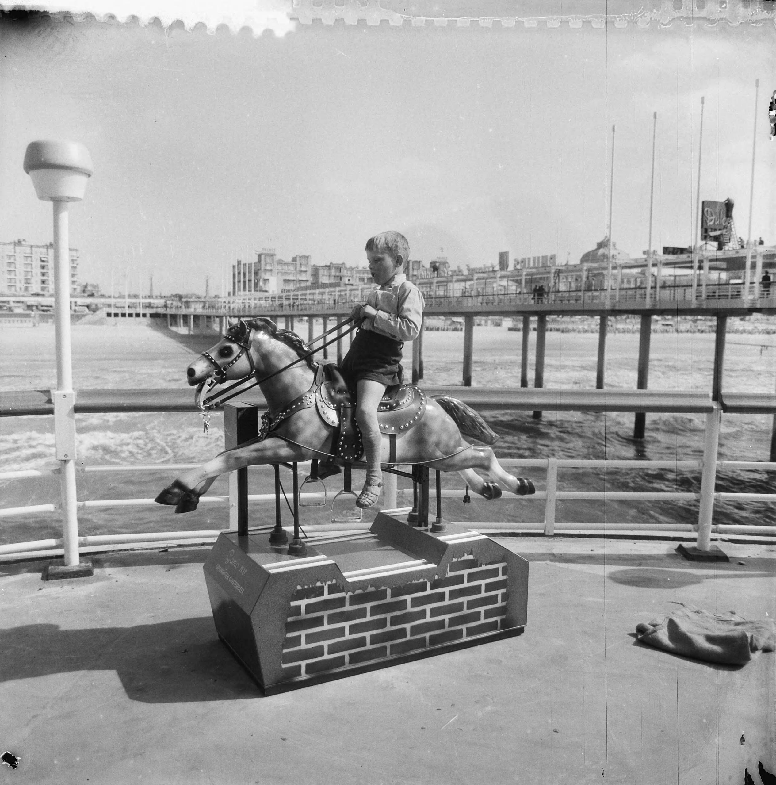 Nieuwe Pier in Scheveningen — Nieuwe Pier in Scheveningen. Elektrisch hobbelpaard — Foto: Nijs, Jac. de / Anefo. Licentie: Set B: Rechtenvrij / Publiek Domein. Bron: Nationaal Archief. http://hdl.handle.net/10648/a9d5b676-d0b4-102d-bcf8-003048976d84