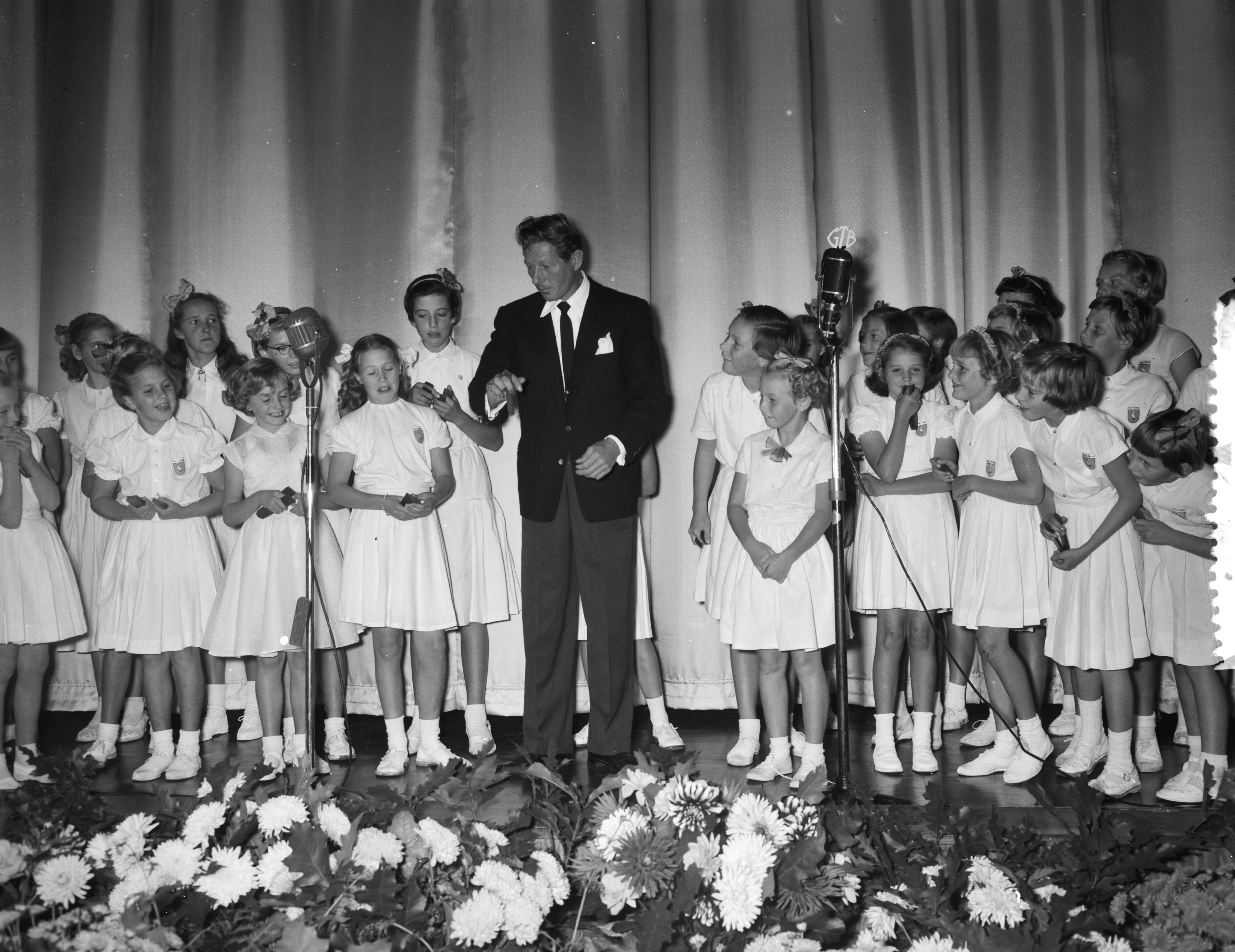 Fotocollectie Anefo — Première van de UNICEF-film "Kinderogen lachen weer" in het Metropole-Tuschinski theater te Den Haag. Danny Kaye kleppert met het kinderkoor "De Haagse Ooievaartjes" — Foto: Noske, J.D. / Anefo. Licentie: Set B: Rechtenvrij / Publiek Domein. Bron: Nationaal Archief. http://hdl.handle.net/10648/a93c5864-d0b4-102d-bcf8-003048976d84