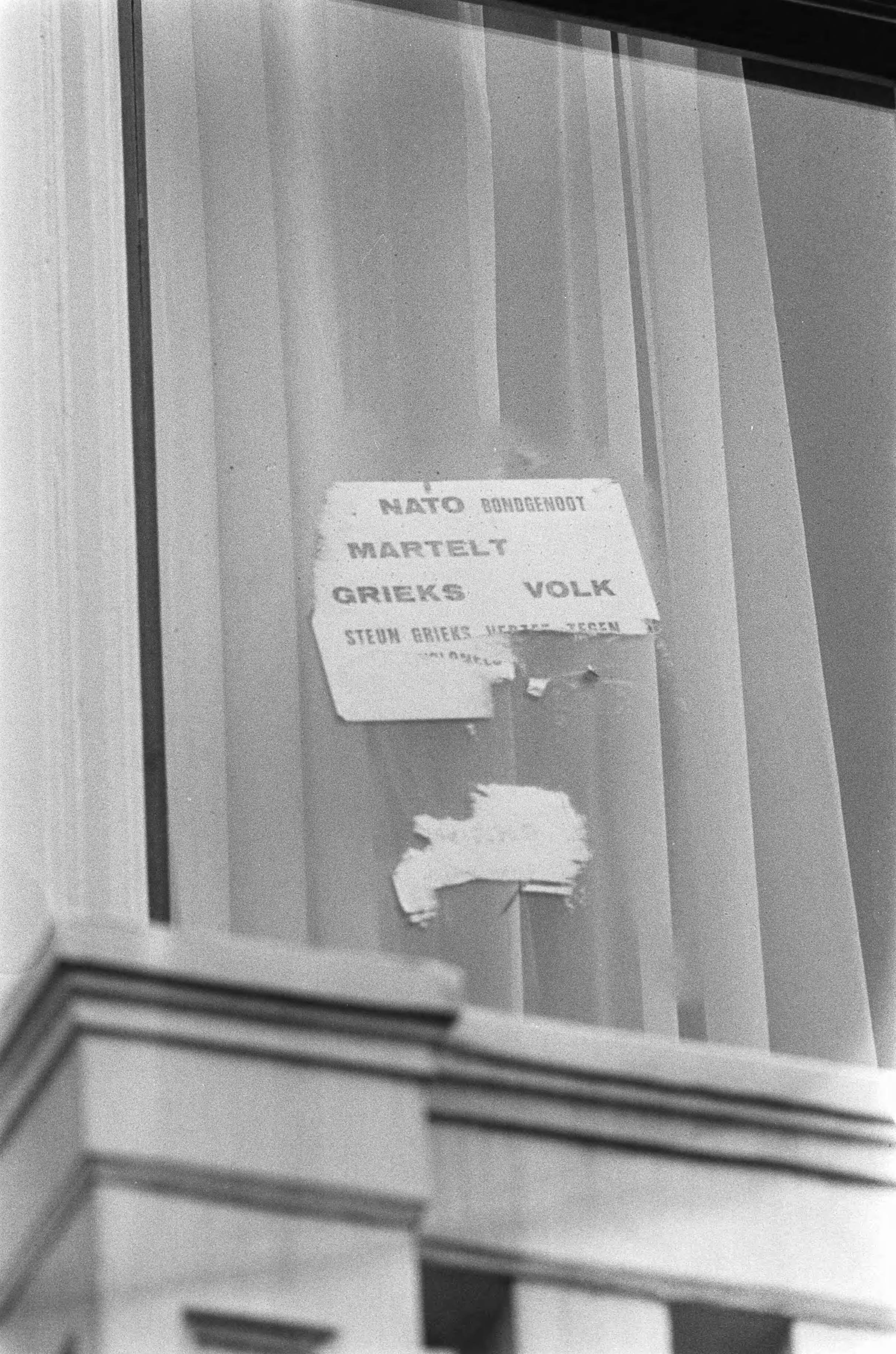 Bezetting van de Griekse ambassade in Den Haag — Een protesttekst die achter een raam werd geplakt, is weer gedeeltelijk verwijderd — Foto: Fotograaf Onbekend / Anefo. Licentie: Set B: Rechtenvrij / Publiek Domein. Bron: Nationaal Archief. http://hdl.handle.net/10648/ac3d4550-d0b4-102d-bcf8-003048976d84