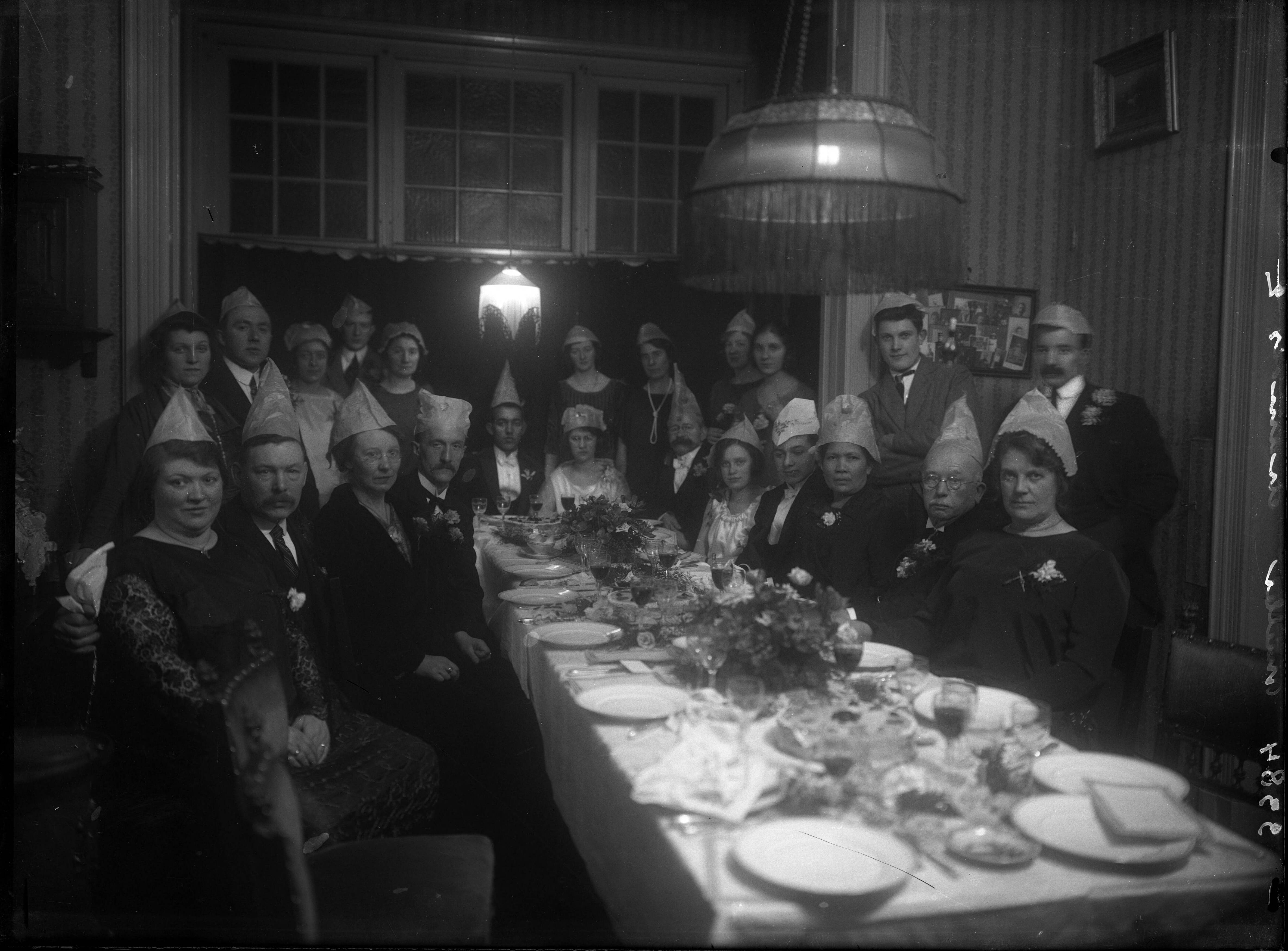 Berg, van den (BERG 050) — Feesten. Zeer donkere opname van een familie met feesthoeden op aan een lange gedekte tafel ter ere van een bruidspaar. Nederland. 1918-1930. 3384 Muller chamois — Foto: Berg, Th.C.J. van den / Spaarnestad Photo (05887). Licentie: Set B: Rechtenvrij / Publiek Domein. Bron: Nationaal Archief. http://hdl.handle.net/10648/35429da7-c776-a382-e063-6df0900a6686