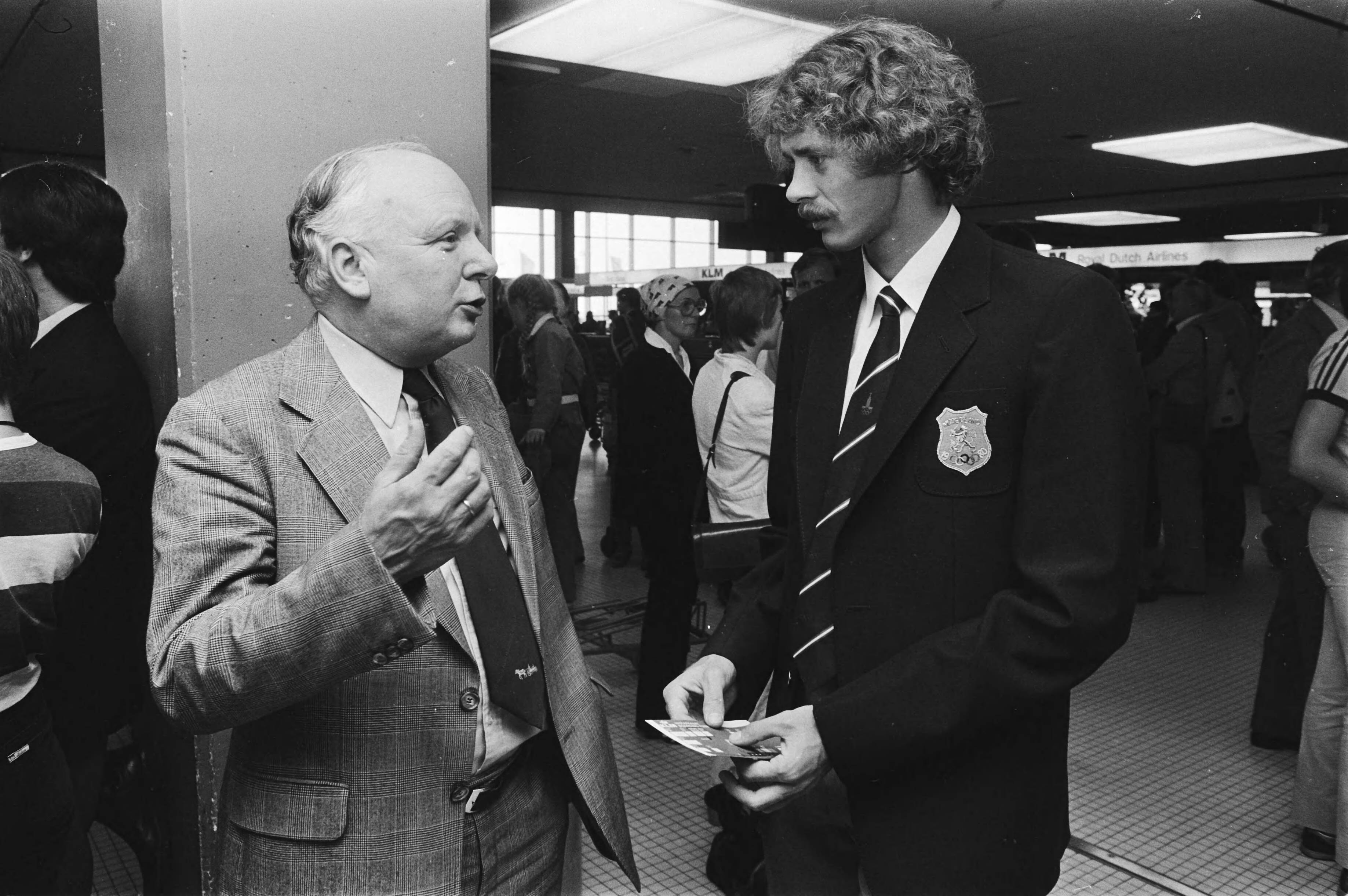 Vertrek gedeelte Olympische atletiekploeg van Schiphol naar Moskou — NOC-voorzitter Idenburg (l) in gesprek met Harry Schulting — Foto: Bogaerts, Rob / Anefo. Licentie: Set B: Rechtenvrij / Publiek Domein. Bron: Nationaal Archief. http://hdl.handle.net/10648/ace467ea-d0b4-102d-bcf8-003048976d84
