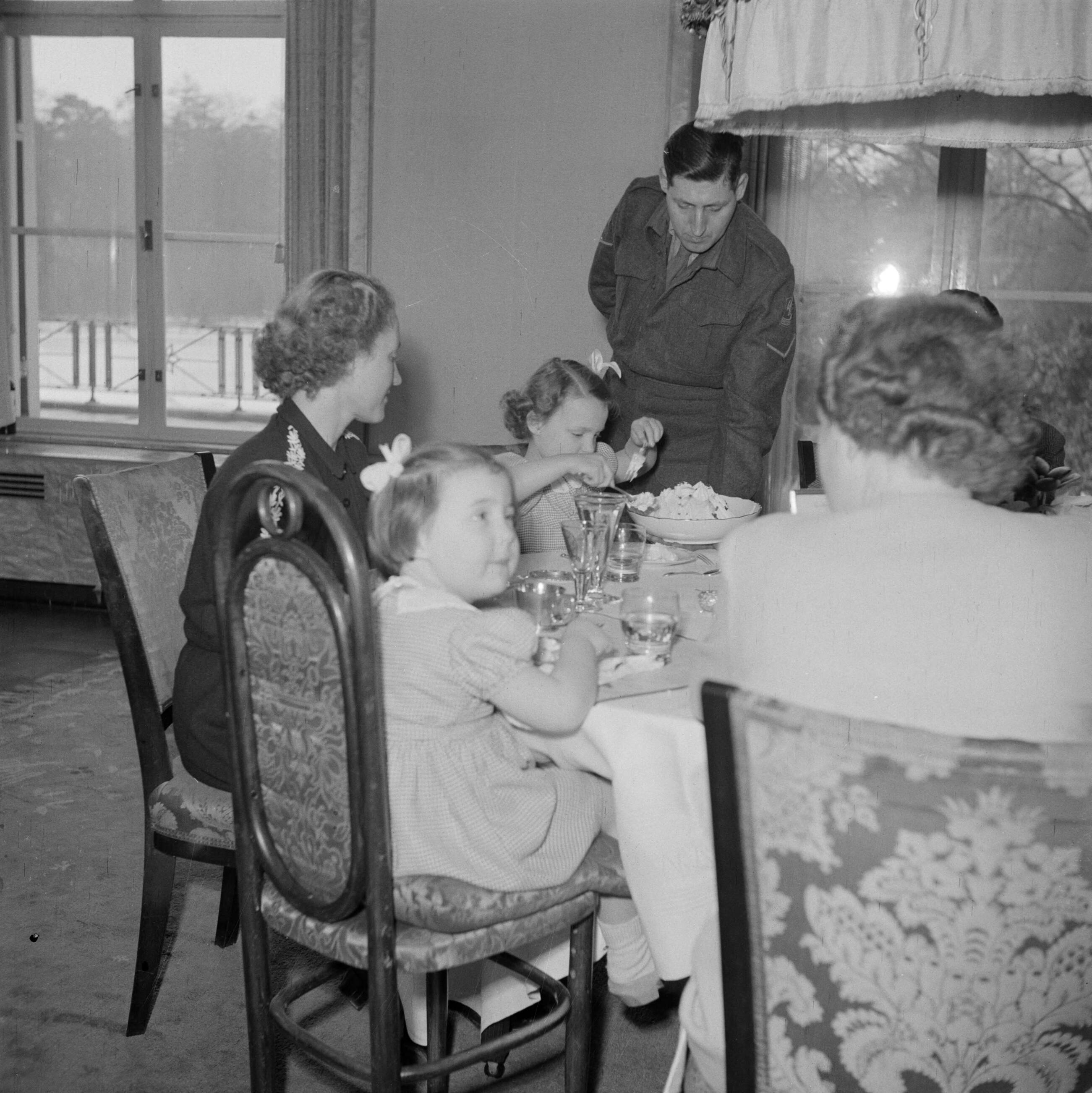 De koninklijke familie op paleis Soestdijk — Prinses Juliana, prins Bernhard, hun dochters en personeelsleden aan de eettafel — Foto: Poll, Willem van de. Licentie: Set B: Rechtenvrij / Publiek Domein. Bron: Nationaal Archief. http://hdl.handle.net/10648/aee92292-d0b4-102d-bcf8-003048976d84