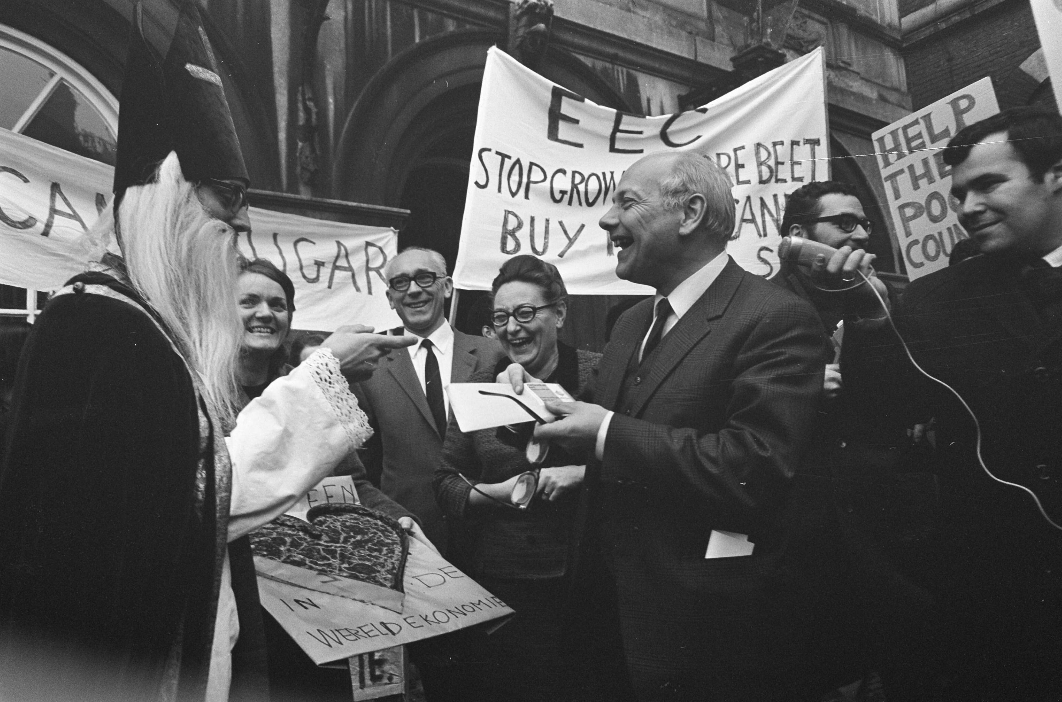 Fotocollectie Anefo — Rietsuikeractie 1968 de demonstranten op het Binnenhof Den Uyl krijgt zakje met rietsuiker — Foto: Kroon, Ron / Anefo. Licentie: Set B: Rechtenvrij / Publiek Domein. Bron: Nationaal Archief. http://hdl.handle.net/10648/ab56c526-d0b4-102d-bcf8-003048976d84