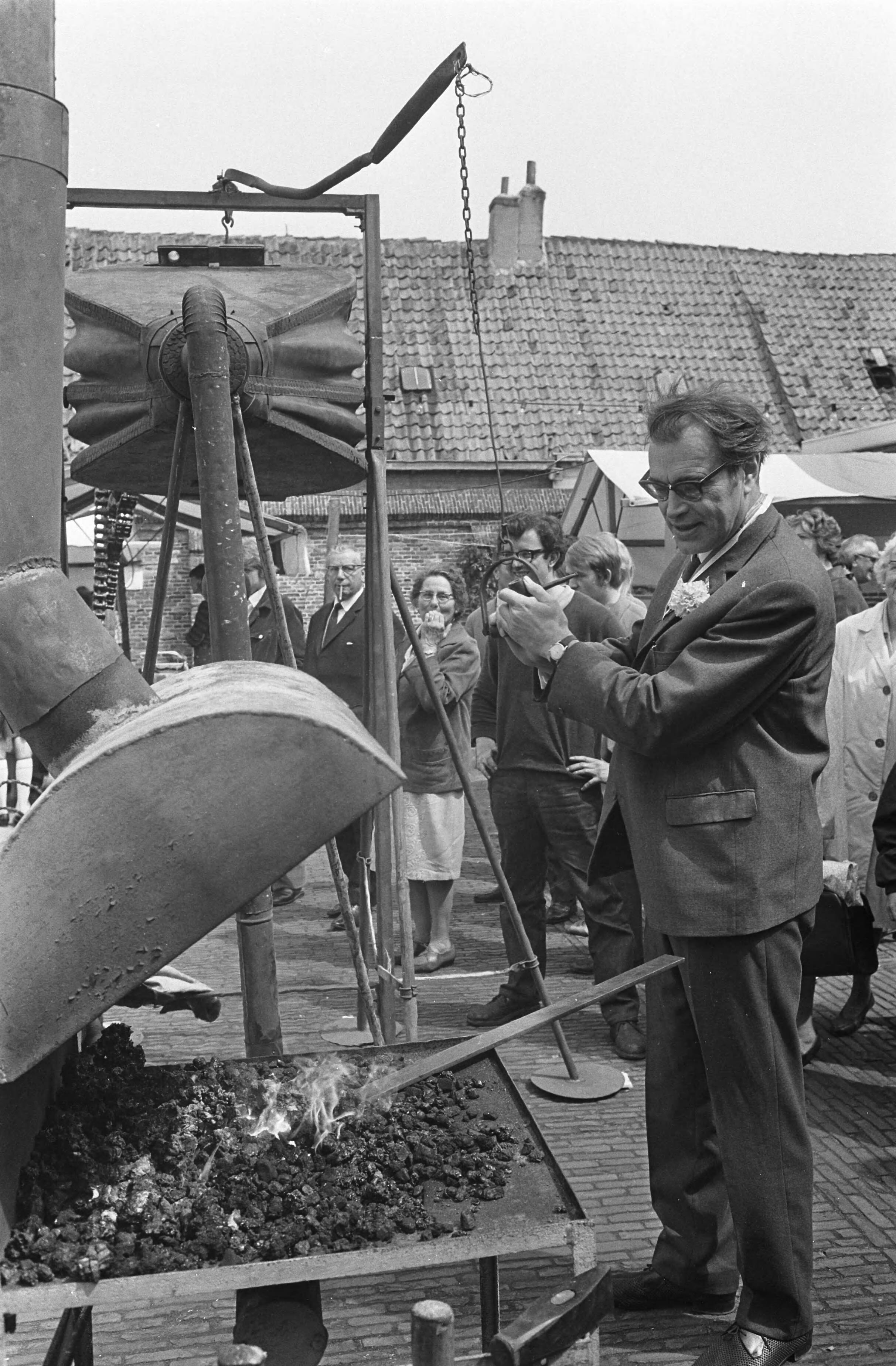 Fotocollectie Anefo — Op de binnenplaats van de Kloveniers- of Stadsdoelen te Haarlem heeft de schrijver Godfried Bomans de 5e Kunstmarkt geopend. Het was ook de vijfde keer dat hij dit mocht doen. Een belangrijk deel van de opbrengst is bestemd voor het gehandicapte kind in Haarlem en omgeving. Na een korte openingsrede hielp Godfried Bomans de siersmid op de markt met het aanwakkeren van het vuur door middel van een grote blaasgalg, waarna kunstenaars aan het werk gingen — Foto: Koch, Eric / Anefo. Licentie: Set B: Rechtenvrij / Publiek Domein. Bron: Nationaal Archief. http://hdl.handle.net/10648/ab437070-d0b4-102d-bcf8-003048976d84