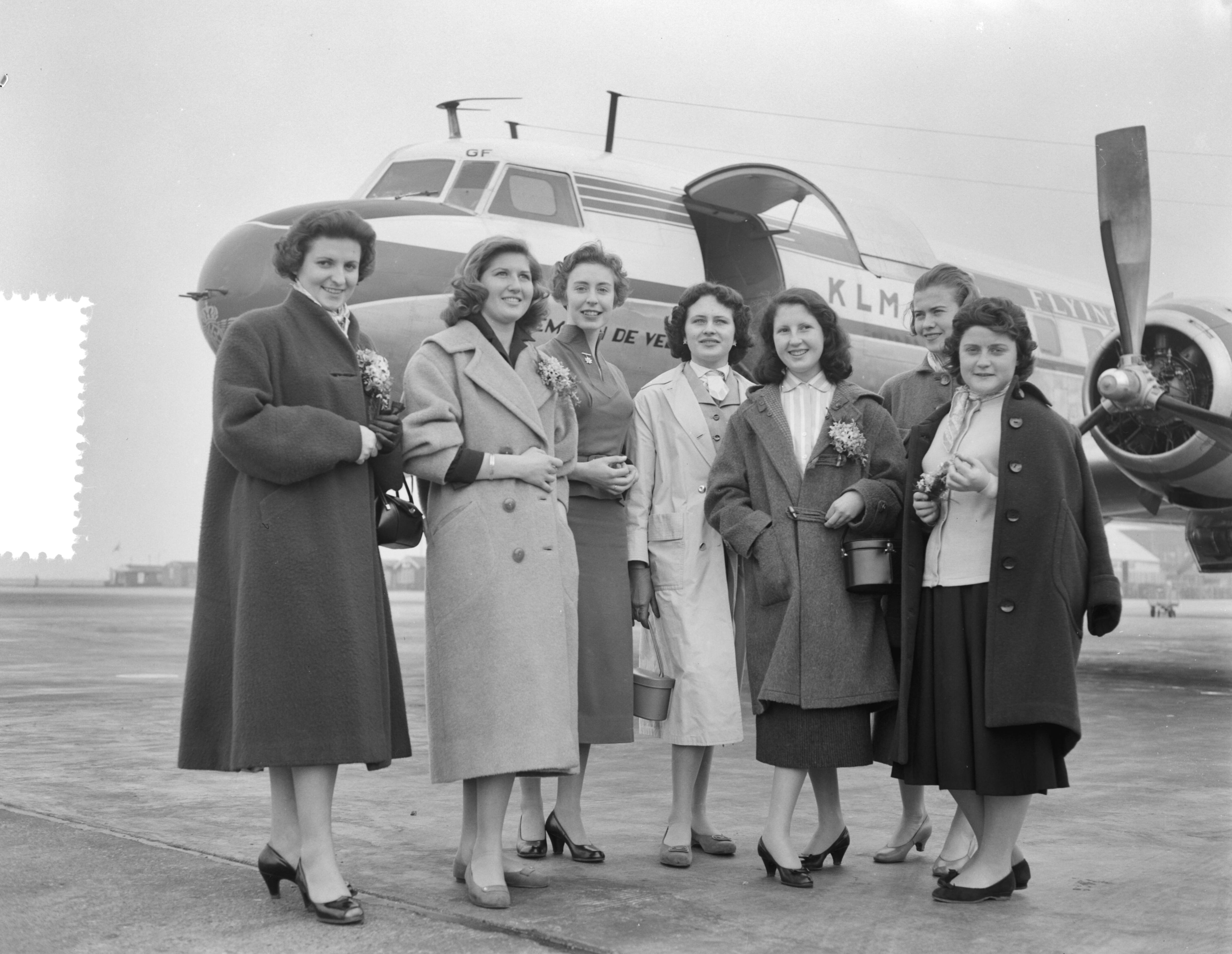 Fotocollectie Anefo — Zes jeugdige Franse meisjes, behorende tot de 20 Françaises, die winnaressen zijn geworden van de wereldcompetitie voor jonge meisjes, uitgeschreven door het Franse damesweekblad „Elle”, zijn met een toestel van de SAS op Schiphol aangekomen. Daar stond het Nederlandse „Doorsnee-meisje” winnares de 20-jarige Mia Kroon uit Hillegom, gereed met corsages samengesteld uit bollenbloemen — Foto: Rossem, Wim van / Anefo. Licentie: Set B: Rechtenvrij / Publiek Domein. Bron: Nationaal Archief. http://hdl.handle.net/10648/ad775122-d0b4-102d-bcf8-003048976d84
