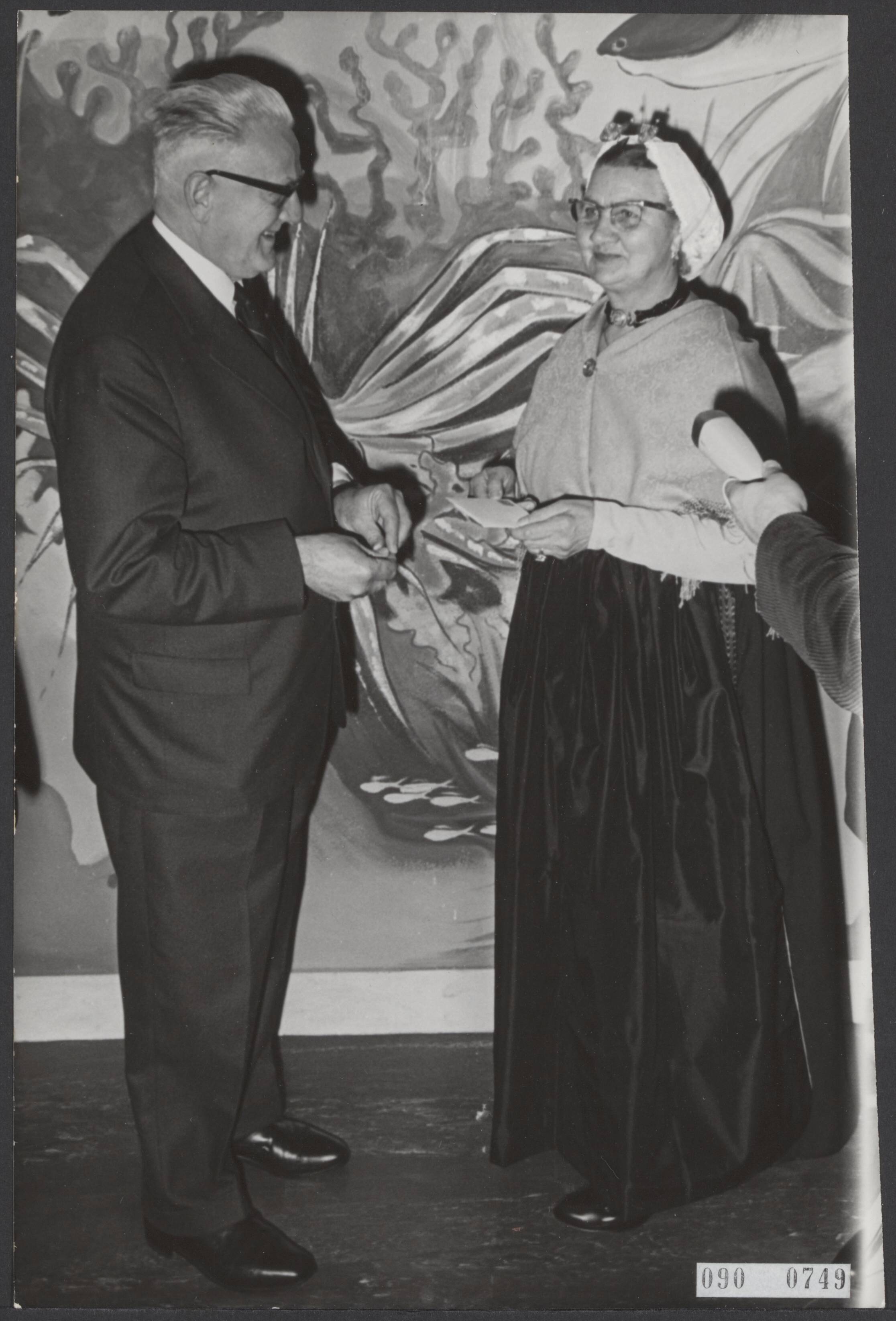 Fotocollectie Elsevier Binnenland — De directeur-generaal van de P.T.T. prof. ir. G.H. Bast heeft de eerste zomerpostzegels verkocht aan mevr. P. Taal-Bal uit Scheveningen. Dit gebeurde in het zeeaquarium aldaar om in de stijl van de afbeeldingen van de zegelserie te blijven, "strandvondsten" waaronder schelpen enz. staan afgebeeld en ontworpen door Auke de Vries. — Foto: Fotograaf Onbekend / Anefo. Licentie: Set B: Rechtenvrij / Publiek Domein. Bron: Nationaal Archief. http://hdl.handle.net/10648/ae1ce060-d0b4-102d-bcf8-003048976d84
