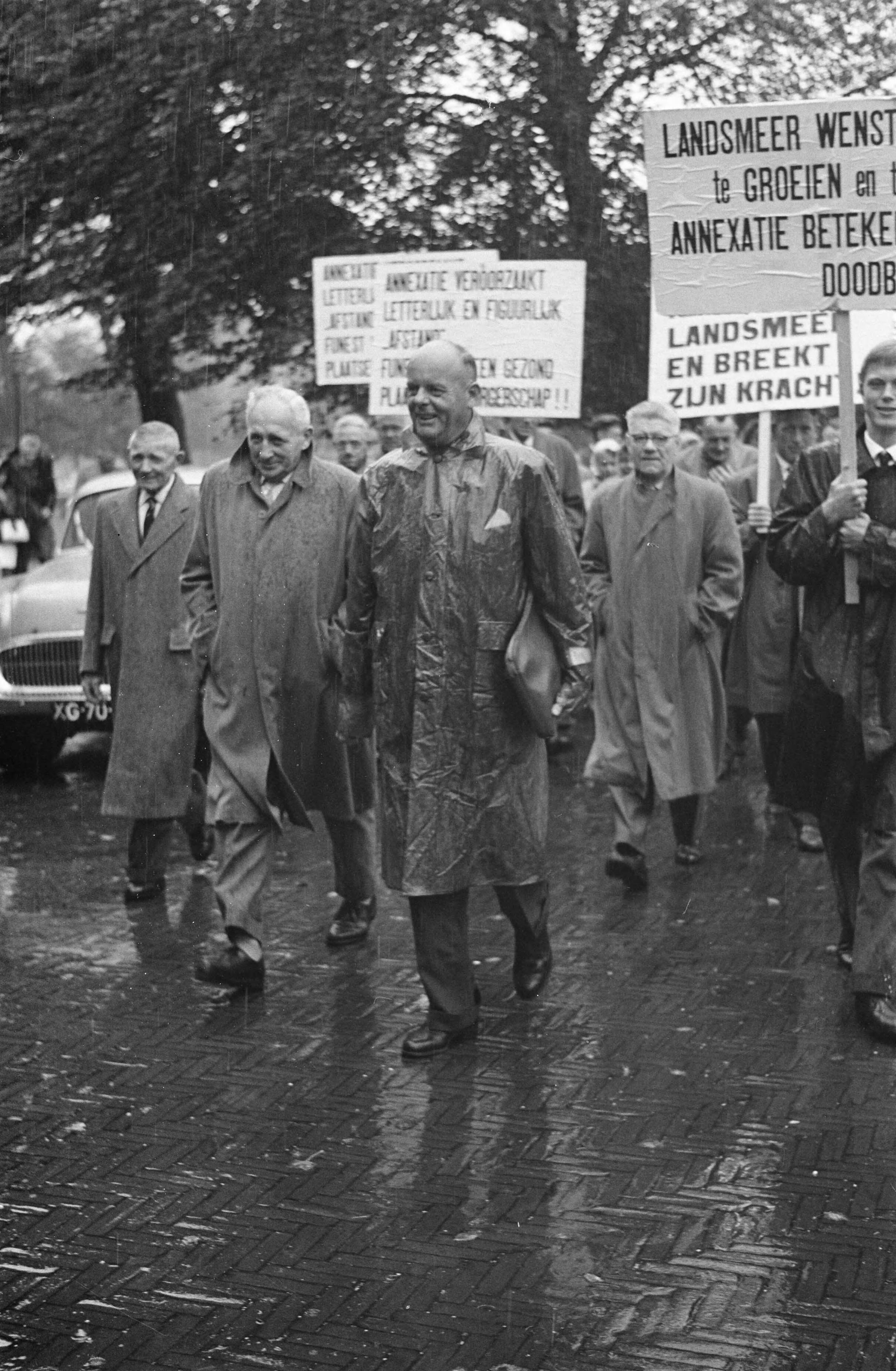 Fotocollectie Anefo — Deputaties uit Landsmeer en Oostzaan protesteren met borden tegen annexatieplannen. Aan het hoofd van de stoet loopt de burgemeester van Landsmeer, G.G. Post — Foto: Pot, Harry / Anefo. Licentie: Set B: Rechtenvrij / Publiek Domein. Bron: Nationaal Archief. http://hdl.handle.net/10648/a9e16980-d0b4-102d-bcf8-003048976d84