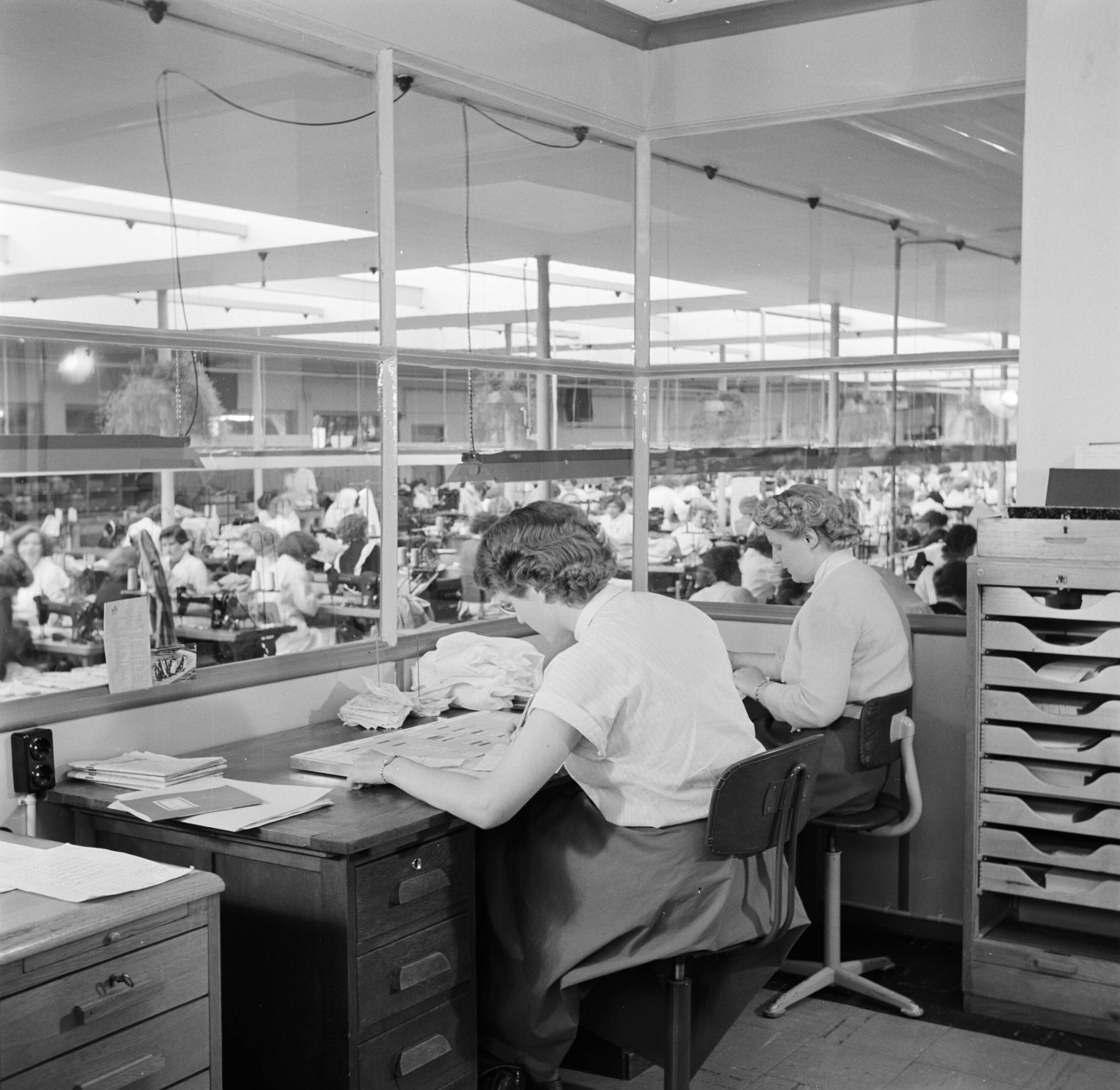 Reportage Kerko Haarlem — De administratie-afdeling van overhemdenbedrijf Kerko met zicht op het naaiatelier — Foto: Poll, Willem van de. Licentie: Set B: Rechtenvrij / Publiek Domein. Bron: Nationaal Archief. http://hdl.handle.net/10648/aecbbba8-d0b4-102d-bcf8-003048976d84
