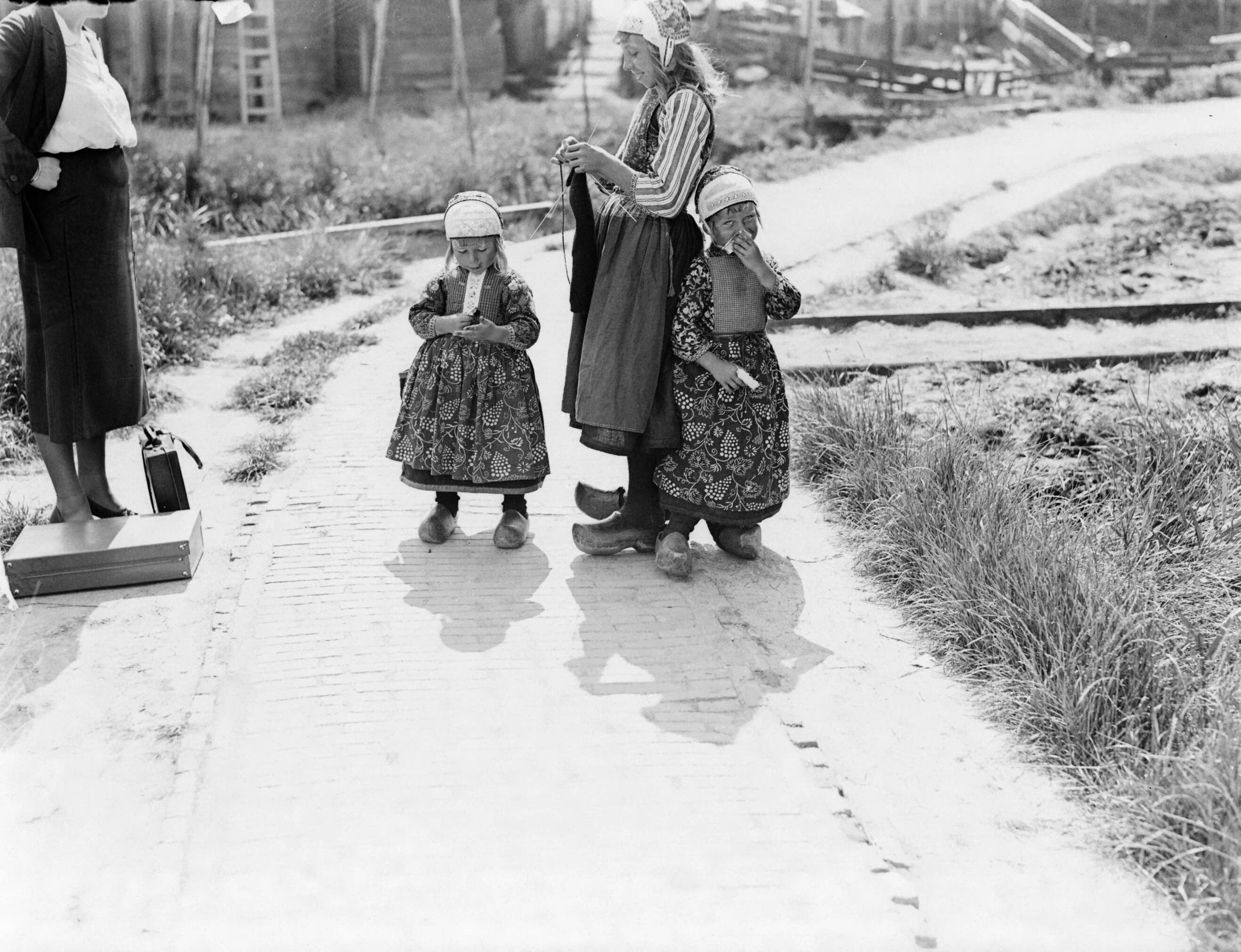 Klederdrachten in Nederland — Drie meisjes in Marker kostuurm. De oudste is aan het breien — Foto: Poll, Willem van de. Licentie: Set B: Rechtenvrij / Publiek Domein. Bron: Nationaal Archief. http://hdl.handle.net/10648/aea7a1be-d0b4-102d-bcf8-003048976d84