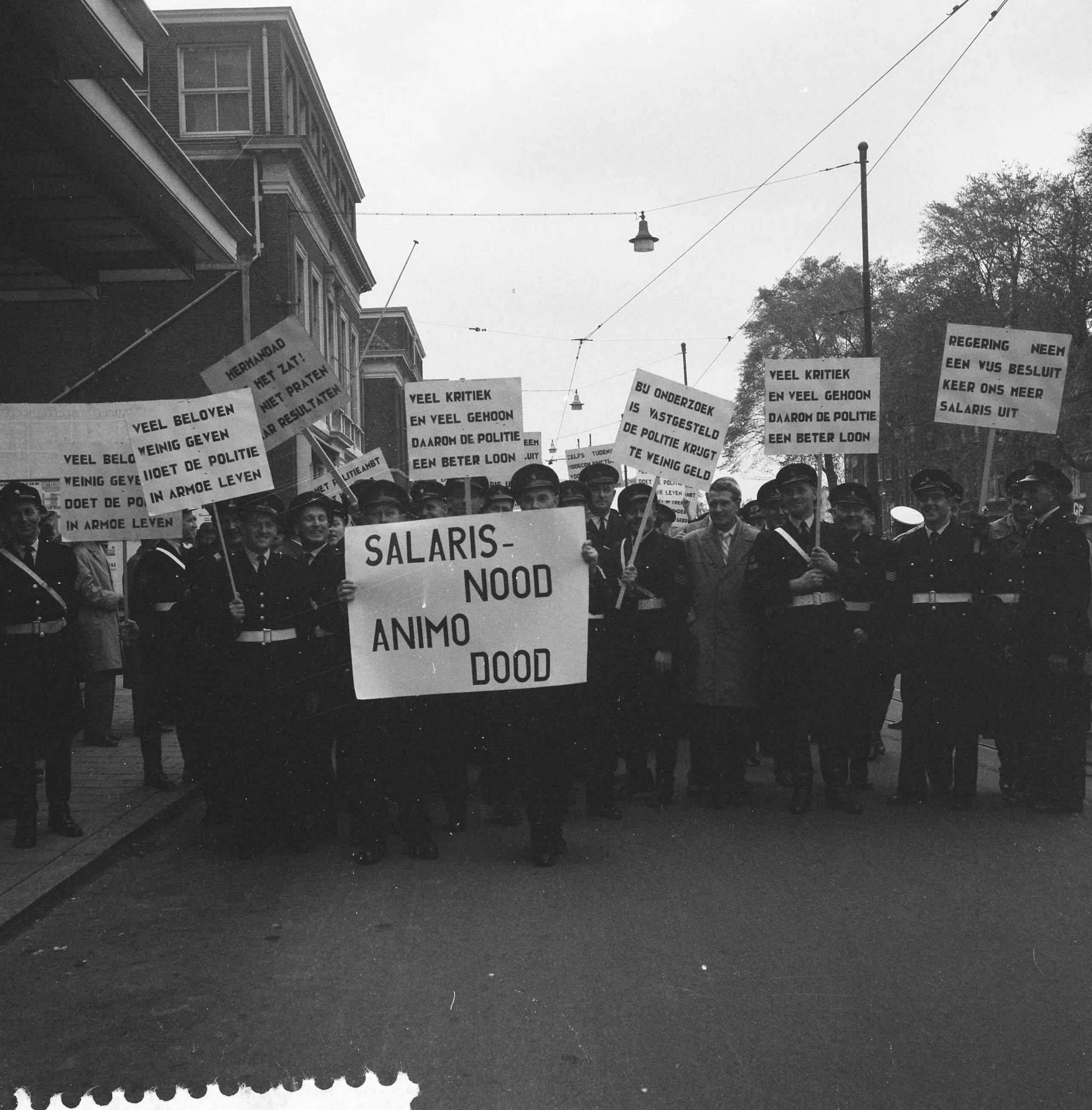 Fotocollectie Anefo — Protestvergadering door politie-ambtenaren tegen loonpolitiek van de regering in het gebouw voor Kunsten en Wetenschappen te Den Haag — Foto: Pot, Harry / Anefo. Licentie: Set B: Rechtenvrij / Publiek Domein. Bron: Nationaal Archief. http://hdl.handle.net/10648/a9bc3f34-d0b4-102d-bcf8-003048976d84