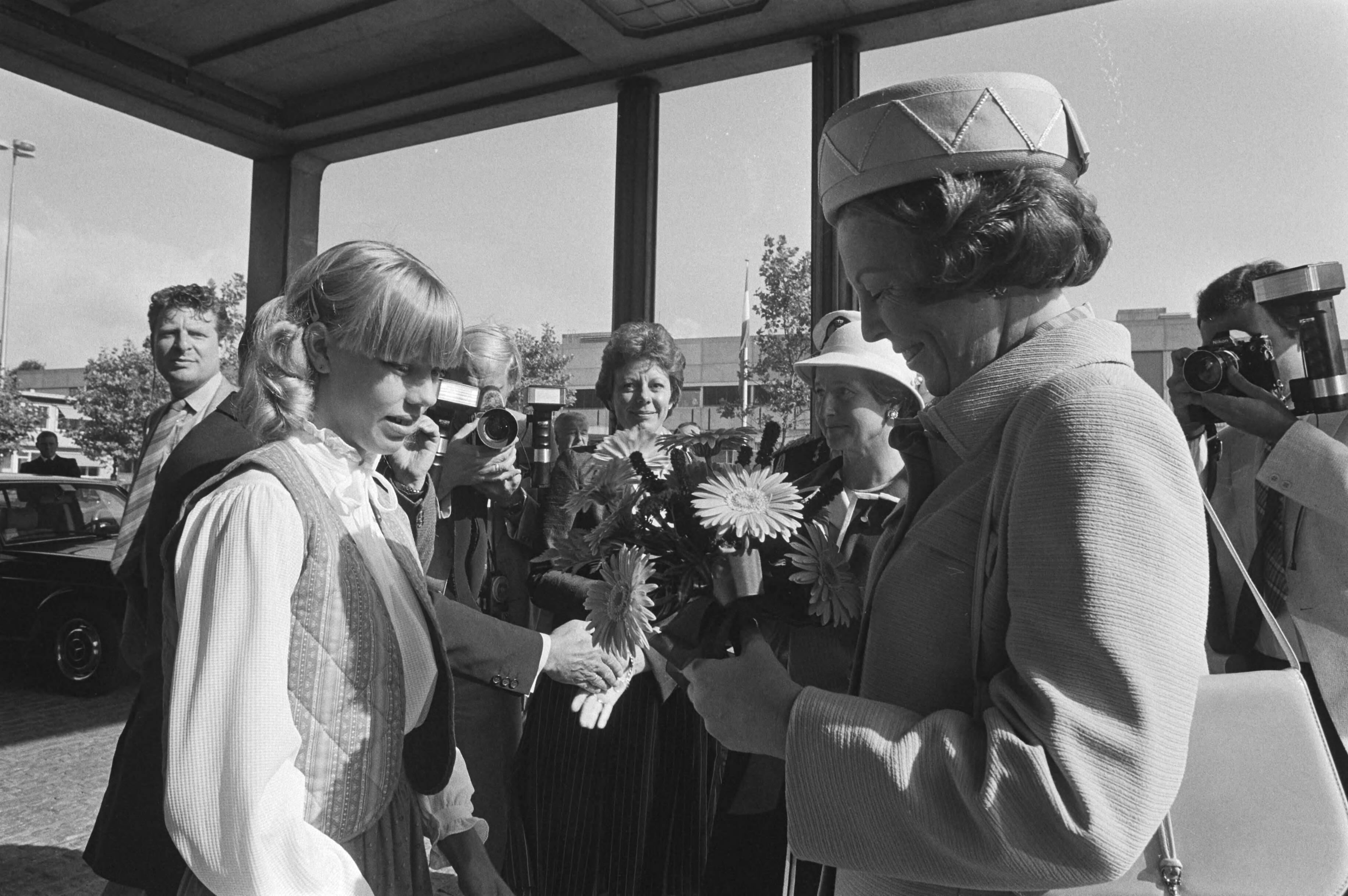 Bezoek van Koningin Beatrix aan de PTT in verband met het 100-jarig bestaan — Koningin Beatrix krijgt bloemen aangeboden door een meisje bij haar bezoek aan de jubilerende PTT — Foto: Dijk, Hans van / Anefo. Licentie: Set B: Rechtenvrij / Publiek Domein. Bron: Nationaal Archief. http://hdl.handle.net/10648/ad02a52a-d0b4-102d-bcf8-003048976d84