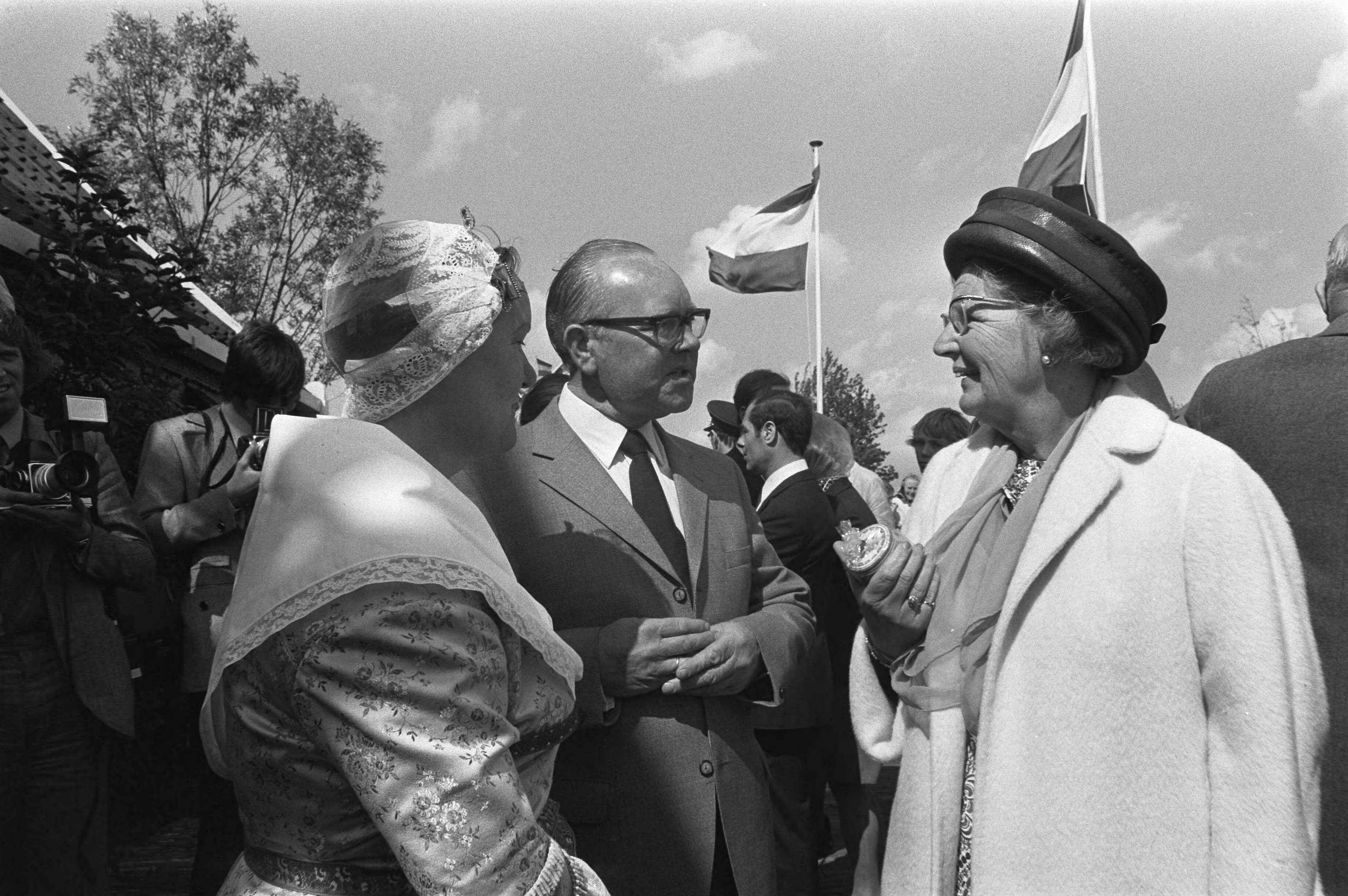 Koningin Juliana op bezoek in de Zaanstreek — Koningin Juliana praat met de heer en mevr. Bosman, mevr. Bosman in Zaanse klederdracht. De heer Bosman was de starter van mosterdmolen De Huisman. De koningin heeft in haar hand een potje Zaanse Mosterd. — Foto: Fotograaf Onbekend / Anefo. Licentie: Set B: Rechtenvrij / Publiek Domein. Bron: Nationaal Archief. http://hdl.handle.net/10648/abec0ad2-d0b4-102d-bcf8-003048976d84