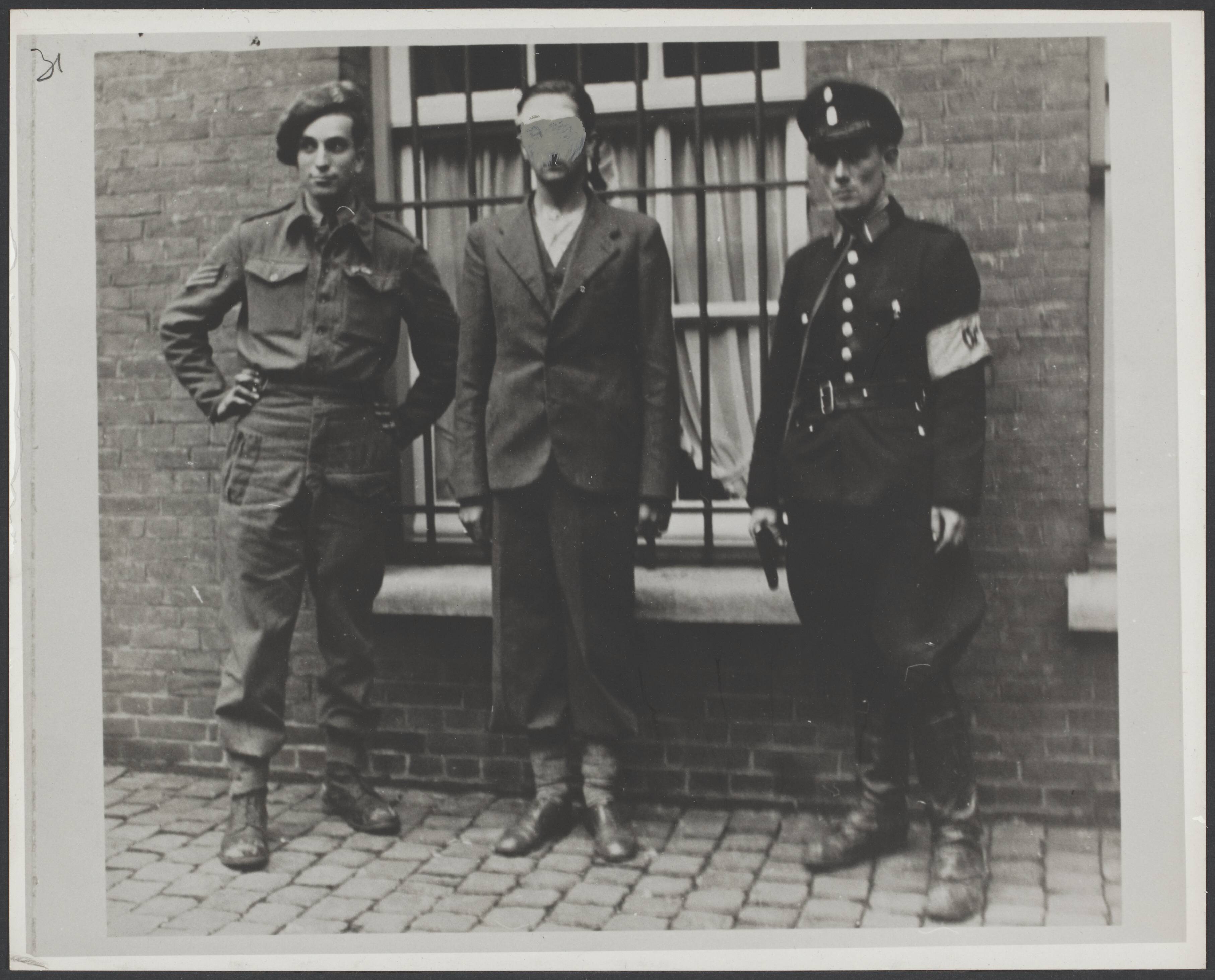 Collaboratie — Maastricht September 1944 [Een gearresteerde collaborateur wordt getoond, geflankeerd door een militair en een politieman] — Foto: Onbekend / RVD. Licentie: Set B: Rechtenvrij / Publiek Domein. Bron: Nationaal Archief. http://hdl.handle.net/10648/4d48c45f-6dce-3f0a-3feb-1ab10835bcb9