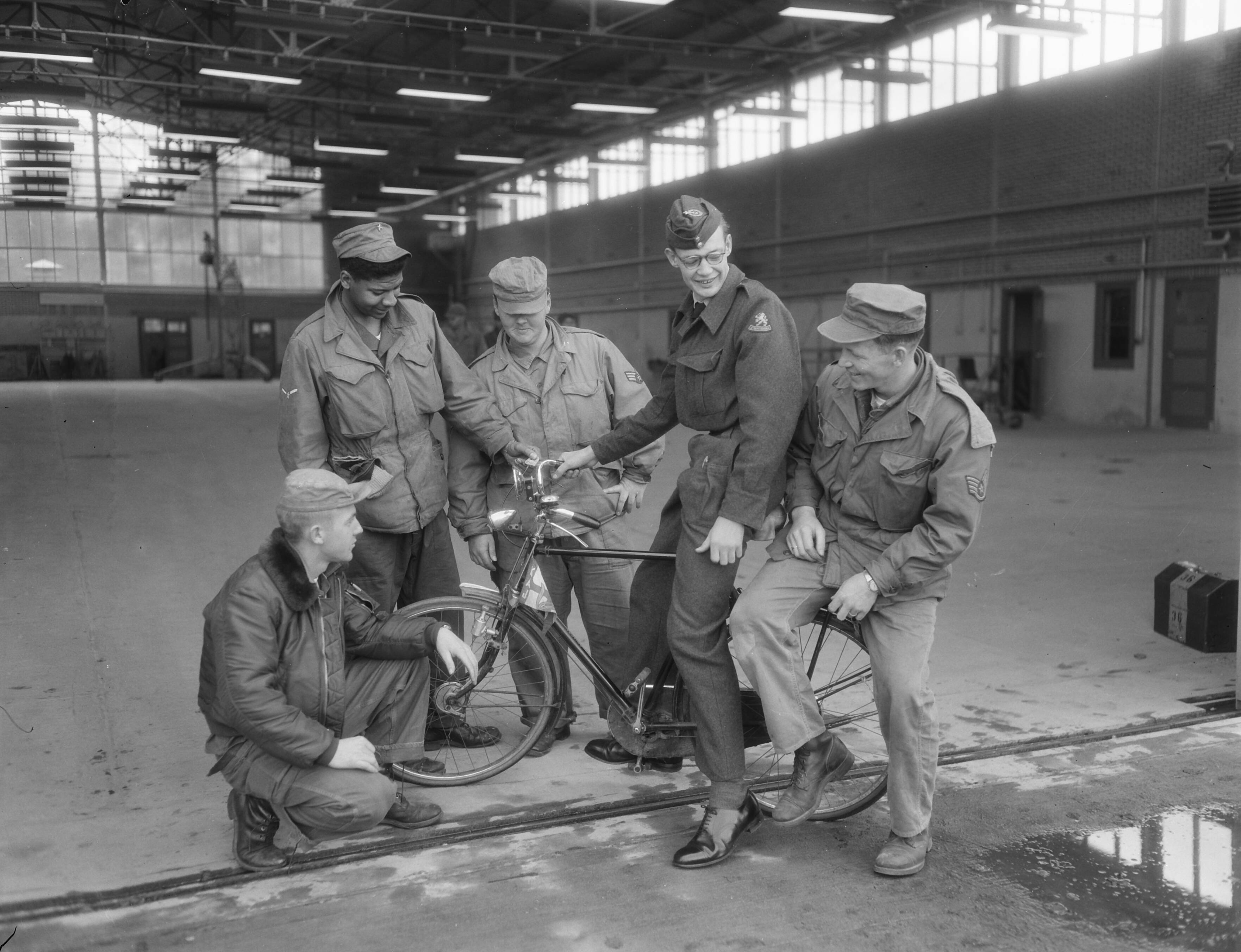 Fotocollectie Anefo — [North American F-86 Sabres van het USAF 32th Fighter Day Squadron gestationeerd op Soesterberg] Nederlandse luchtmachtmilitair op fiets met Amerikanen — Foto: Duinen, G.W. van / Anefo. Licentie: Set B: Rechtenvrij / Publiek Domein. Bron: Nationaal Archief. http://hdl.handle.net/10648/a92cb008-d0b4-102d-bcf8-003048976d84