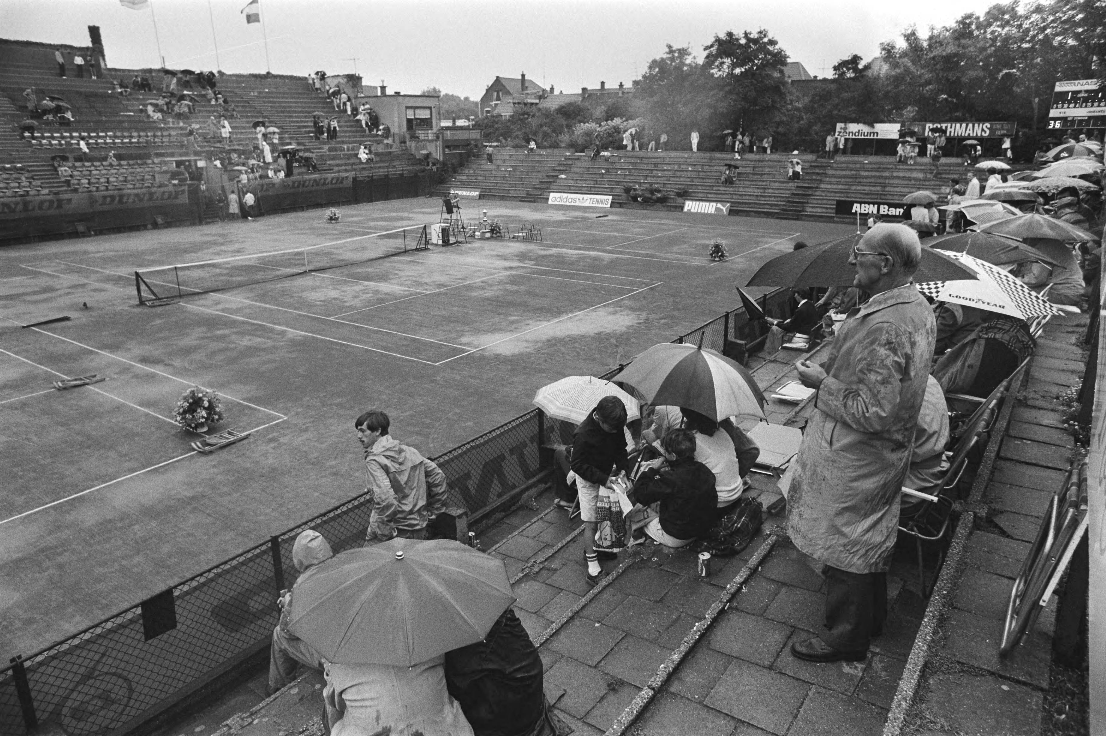 Fotocollectie Anefo — Nationale tenniskampioenschappen, Scheveningen; publiek in de regen op METS-baan — Foto: Croes, Rob C. / Anefo. Licentie: Set B: Rechtenvrij / Publiek Domein. Bron: Nationaal Archief. http://hdl.handle.net/10648/ad1c9692-d0b4-102d-bcf8-003048976d84