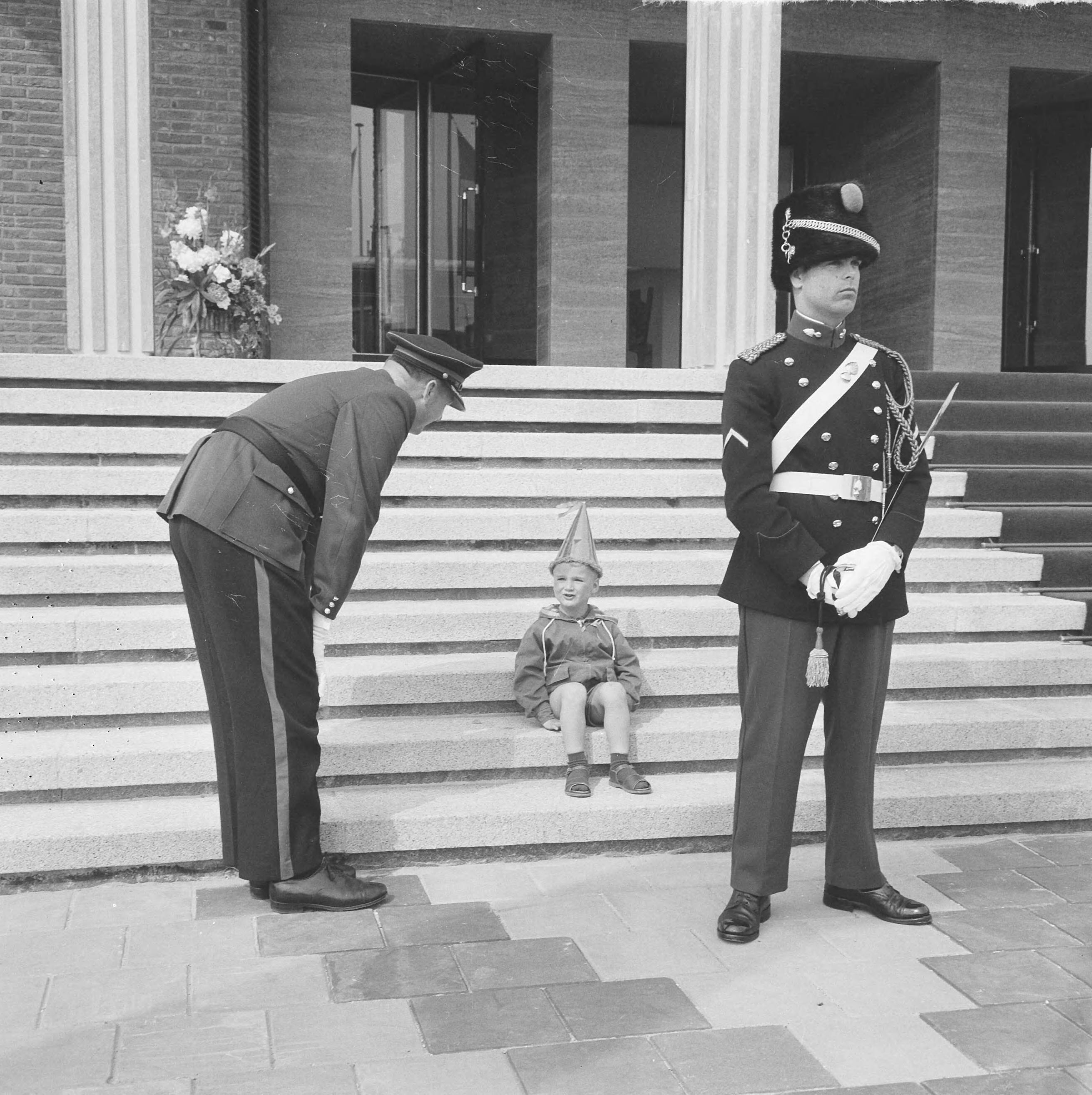 Koningin Juliana opent het nieuwe stadhuis te Vlissingen — Een jongetje met feestmuts zit op de trappen van het stadhuis. Voor hem een marechaussee. Links een politieagent — Foto: Nijs, Jac. de / Anefo. Licentie: Set B: Rechtenvrij / Publiek Domein. Bron: Nationaal Archief. http://hdl.handle.net/10648/5def14cc-6f99-dc23-ccee-1897898a0de7