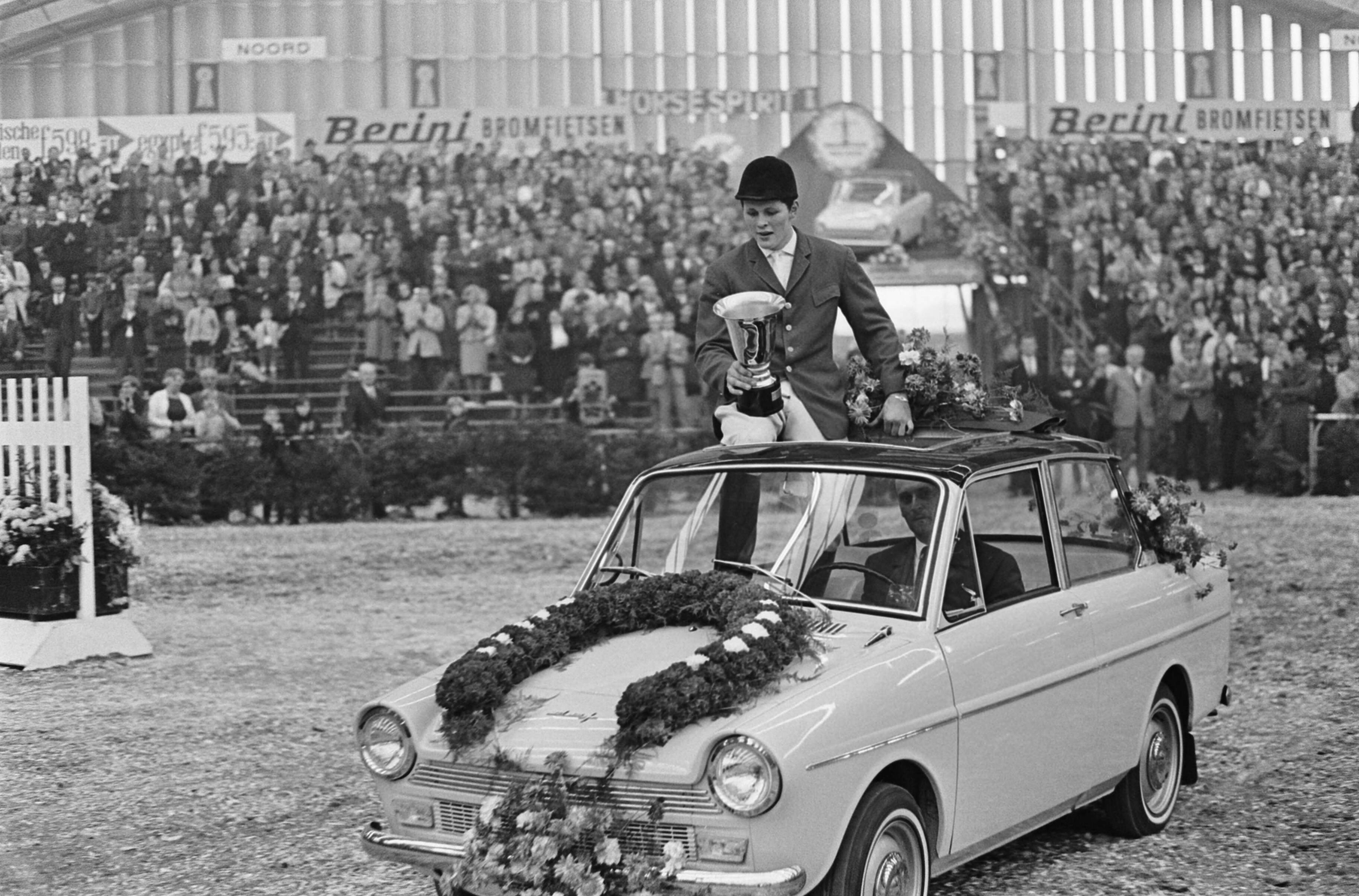 Jumping Amsterdam 1965 in de RAI te Amsterdam — Winnaar van Grote Prijs van Amsterdam, Gerd Wiltfang, tijdens zijn huldiging bij een Daf-personenauto (opdracht DAF) — Foto: Fotograaf Onbekend / Anefo. Licentie: Set B: Rechtenvrij / Publiek Domein. Bron: Nationaal Archief. http://hdl.handle.net/10648/aac8ea3a-d0b4-102d-bcf8-003048976d84