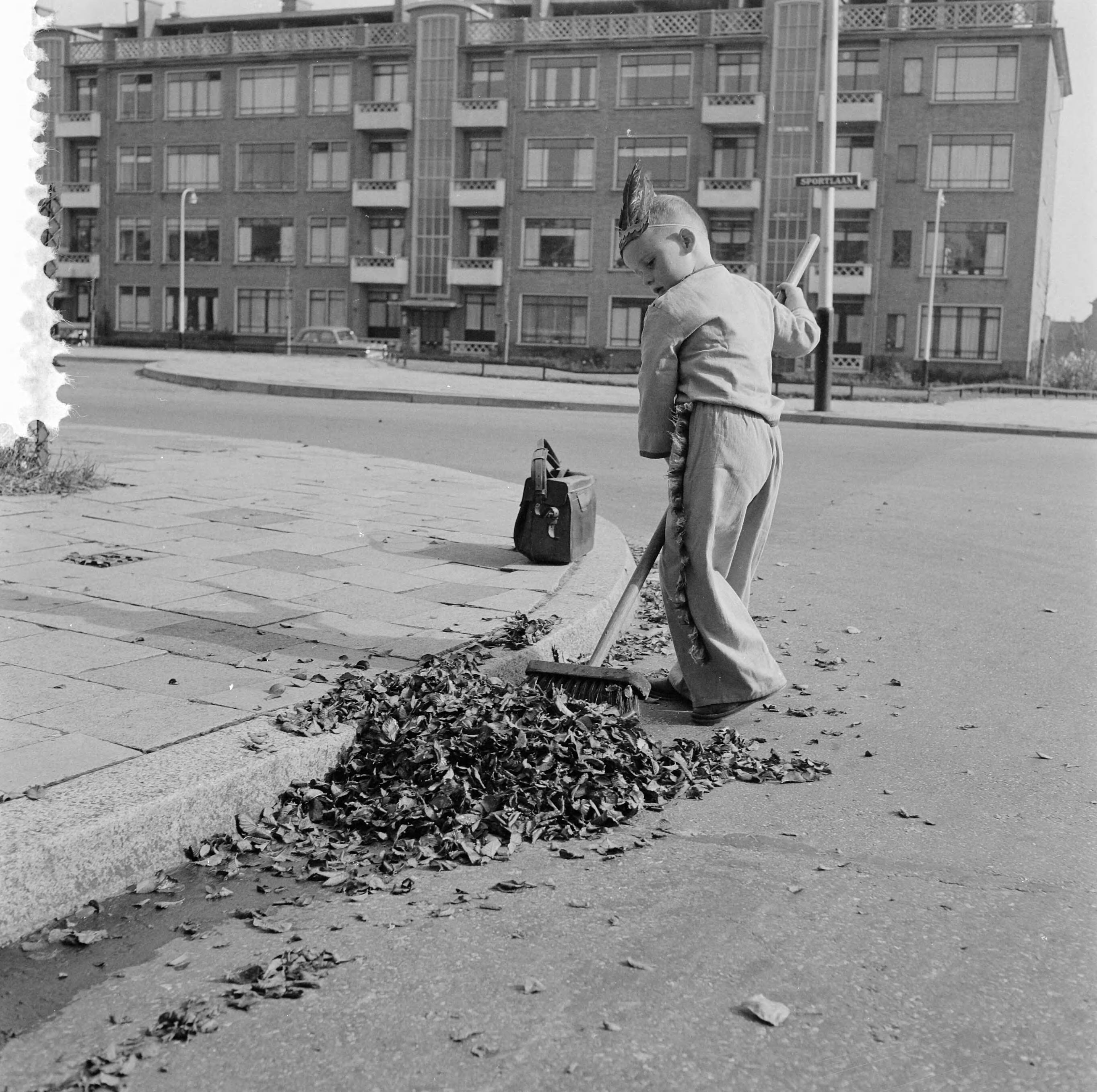 Fotocollectie Anefo — Jongetje, verkleed als Indiaan, dat bladeren wegveegt aan de Sportlaan te Den Haag — Foto: Behrens, Herbert F. / Anefo. Licentie: Set B: Rechtenvrij / Publiek Domein. Bron: Nationaal Archief. http://hdl.handle.net/10648/a96aee22-d0b4-102d-bcf8-003048976d84