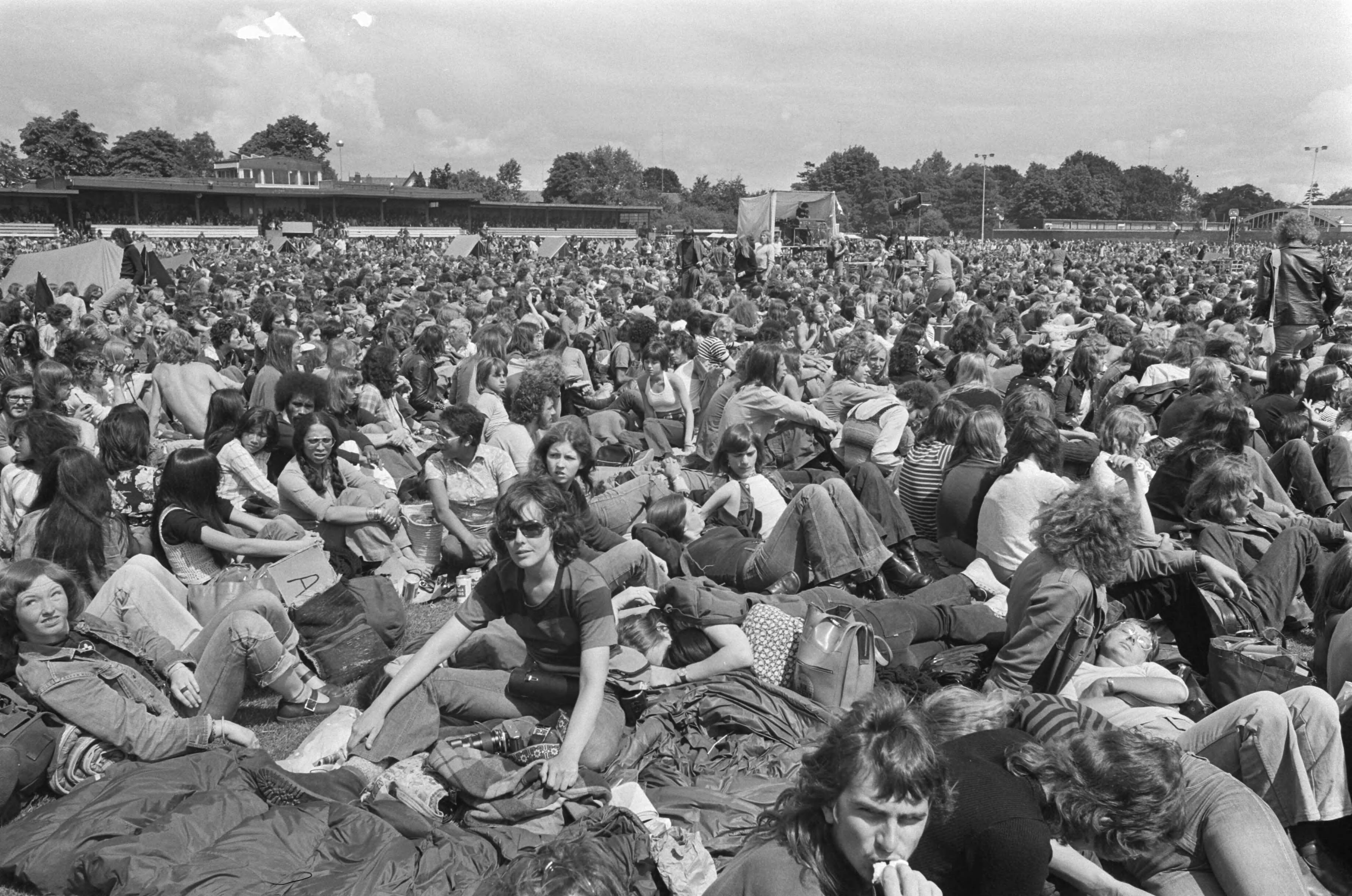Fotocollectie Anefo — Internationaal Popfestival in Hilversum; op de grond gezeten menigte toeschouwers — Foto: Verhoeff, Bert / Anefo. Licentie: Set B: Rechtenvrij / Publiek Domein. Bron: Nationaal Archief. http://hdl.handle.net/10648/ac50aef6-d0b4-102d-bcf8-003048976d84