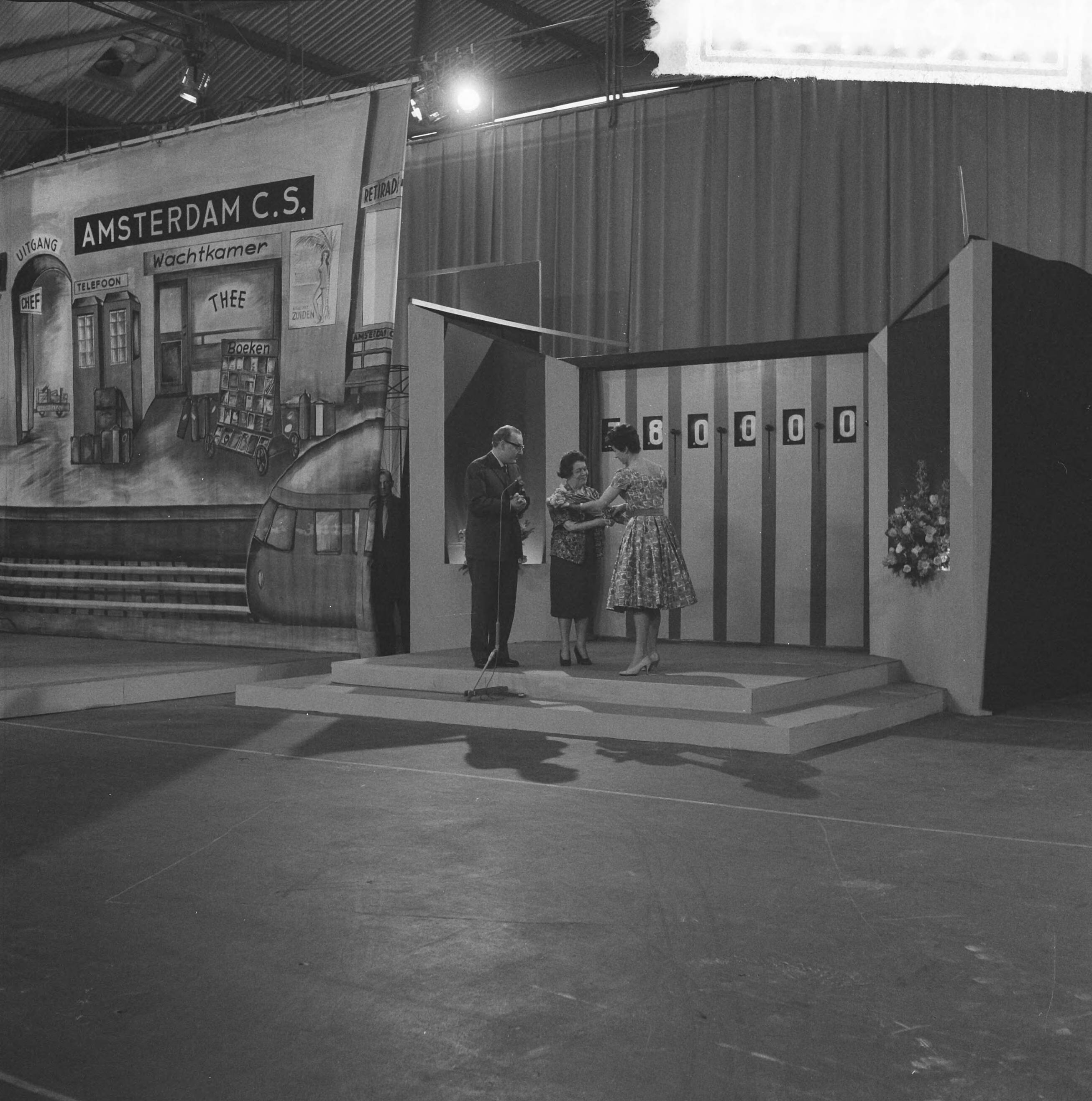 Fotocollectie Anefo — Televisieprogramma "TV-Toto" vanuit de Expohal te Hilversum. Vlnr. presentator Theo Eerdmans, Julia de Gruyter en assistente Maud — Foto: Lindeboom, Henk / Anefo. Licentie: Set B: Rechtenvrij / Publiek Domein. Bron: Nationaal Archief. http://hdl.handle.net/10648/a9d348aa-d0b4-102d-bcf8-003048976d84