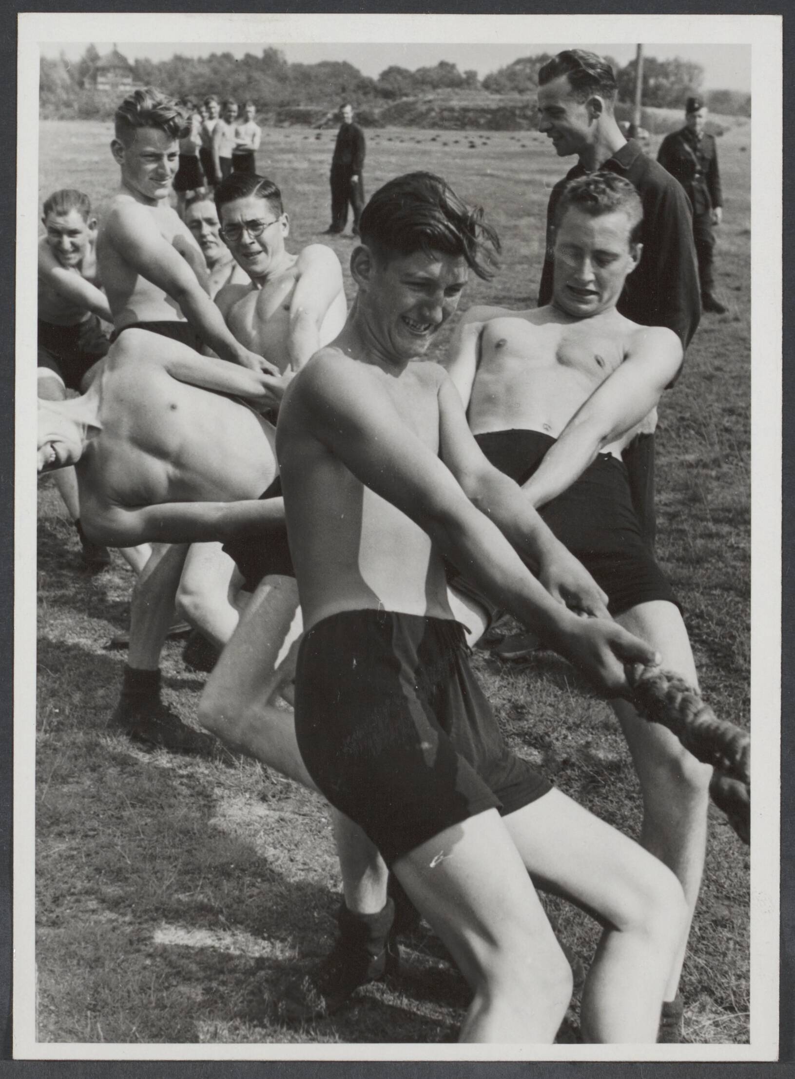 Arbeidsdienst. Waaronder "Nederlandse Arbeidsdienst" en "Vreugde en Arbeid" ("Fut door lol" 81). Ook opbouwdienst 1940/41. — De eerste groep vrijwilligers van de Nederlandse Arbeidsdienst is na 6 maanden scholing afgezwaaid. De gezonde bruingebrande jongens meten hun krachten met hun kameraden bij het touwtrekken — Foto: Mol, W.F.M. / Stapf Bilderdienst (1). Licentie: Set B: Rechtenvrij / Publiek Domein. Bron: Nationaal Archief. http://hdl.handle.net/10648/fa2869f1-0c14-3a0a-c48f-39bb68512b1d