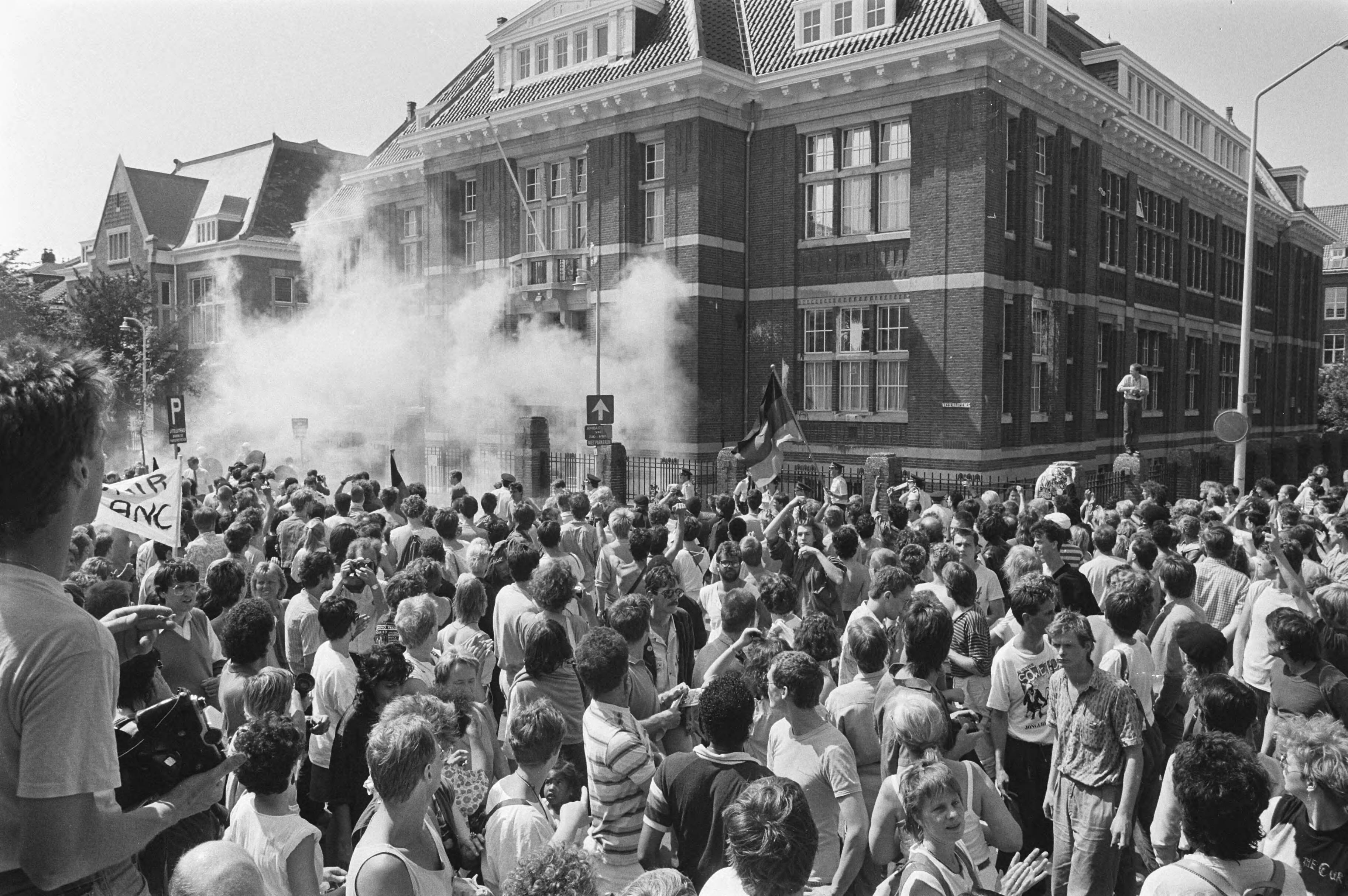 Fotocollectie Anefo — Demonstratie in Den Haag naar aanleiding van 10-jarige opstand in Soweto; rookwolken rond Zuid-Afrikaanse ambassade — Foto: Croes, Rob C. / Anefo. Licentie: Set B: Rechtenvrij / Publiek Domein. Bron: Nationaal Archief. http://hdl.handle.net/10648/ad5464b4-d0b4-102d-bcf8-003048976d84