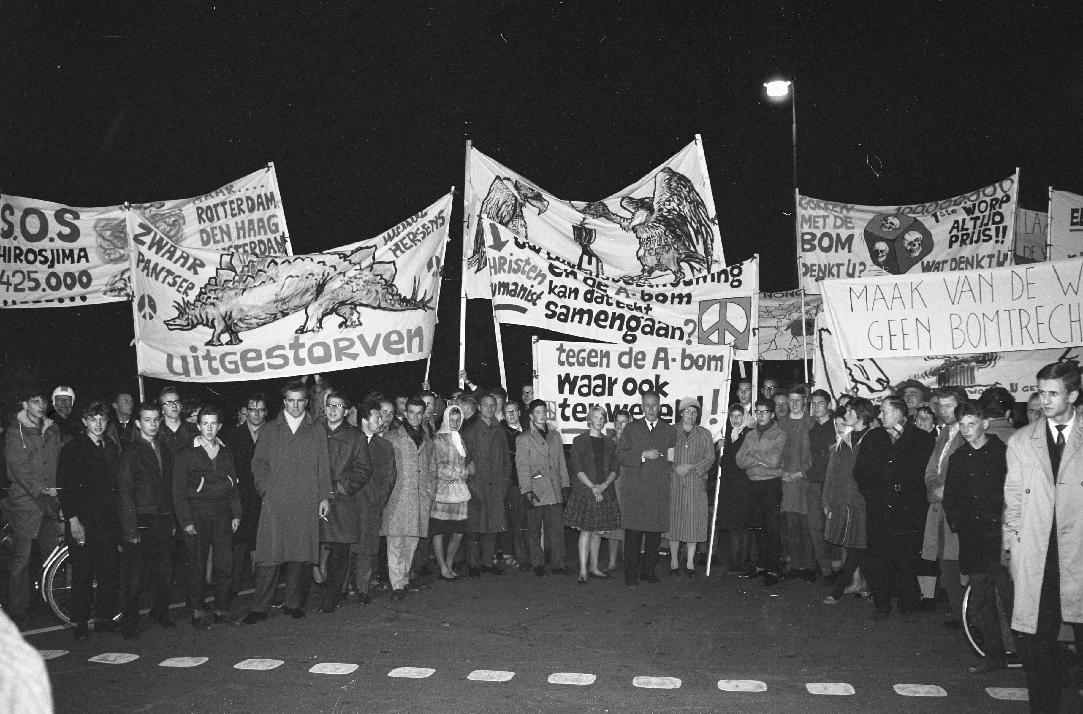 Fotocollectie Anefo — Betogers met spandoeken tijdens een anti-atoombomdemonstratie in Den Haag — Foto: Boer, […] de / Anefo. Licentie: Set B: Rechtenvrij / Publiek Domein. Bron: Nationaal Archief. http://hdl.handle.net/10648/a9e99a38-d0b4-102d-bcf8-003048976d84