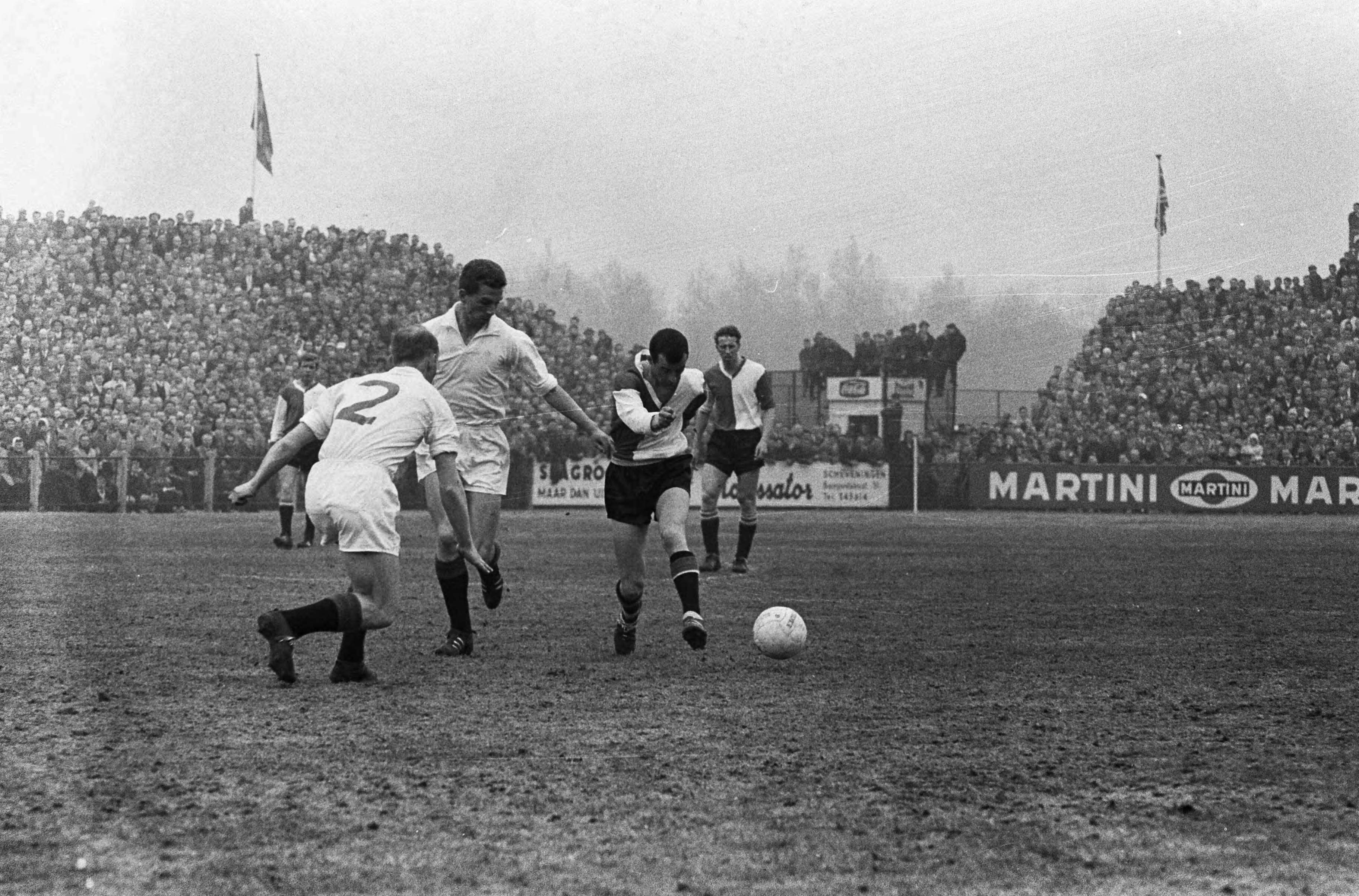 Fotocollectie Anefo — Voetbal. ADO tegen Feijenoord 1-1, Spelmoment, Coen Moulijn schiet, hij wordt op de huid gezeten door Guus Haak. Op de rug gezien Jan Verhoek — Foto: Koch, Eric / Anefo. Licentie: Set B: Rechtenvrij / Publiek Domein. Bron: Nationaal Archief. http://hdl.handle.net/10648/aa3429c2-d0b4-102d-bcf8-003048976d84