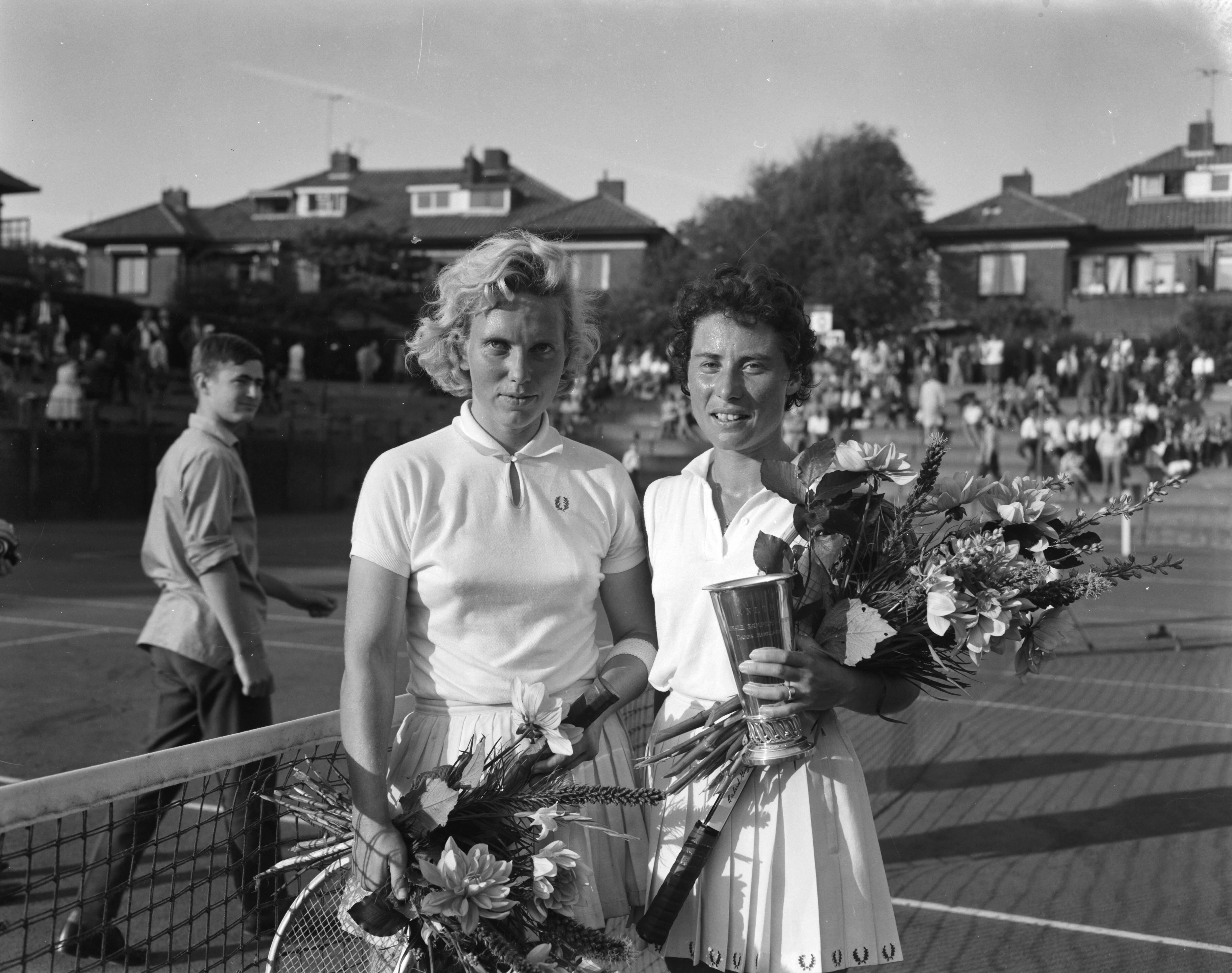 Fotocollectie Anefo — Nederlandse tenniskampioenschappen gespeeld op de METS-banen te Scheveningen. Eva de Jong, kampioen dames enkel en haar tegenstandster in de finale Jetty Baars-Wienese (links) — Foto: Bilsen, Joop van / Anefo. Licentie: Set B: Rechtenvrij / Publiek Domein. Bron: Nationaal Archief. http://hdl.handle.net/10648/aa1439aa-d0b4-102d-bcf8-003048976d84